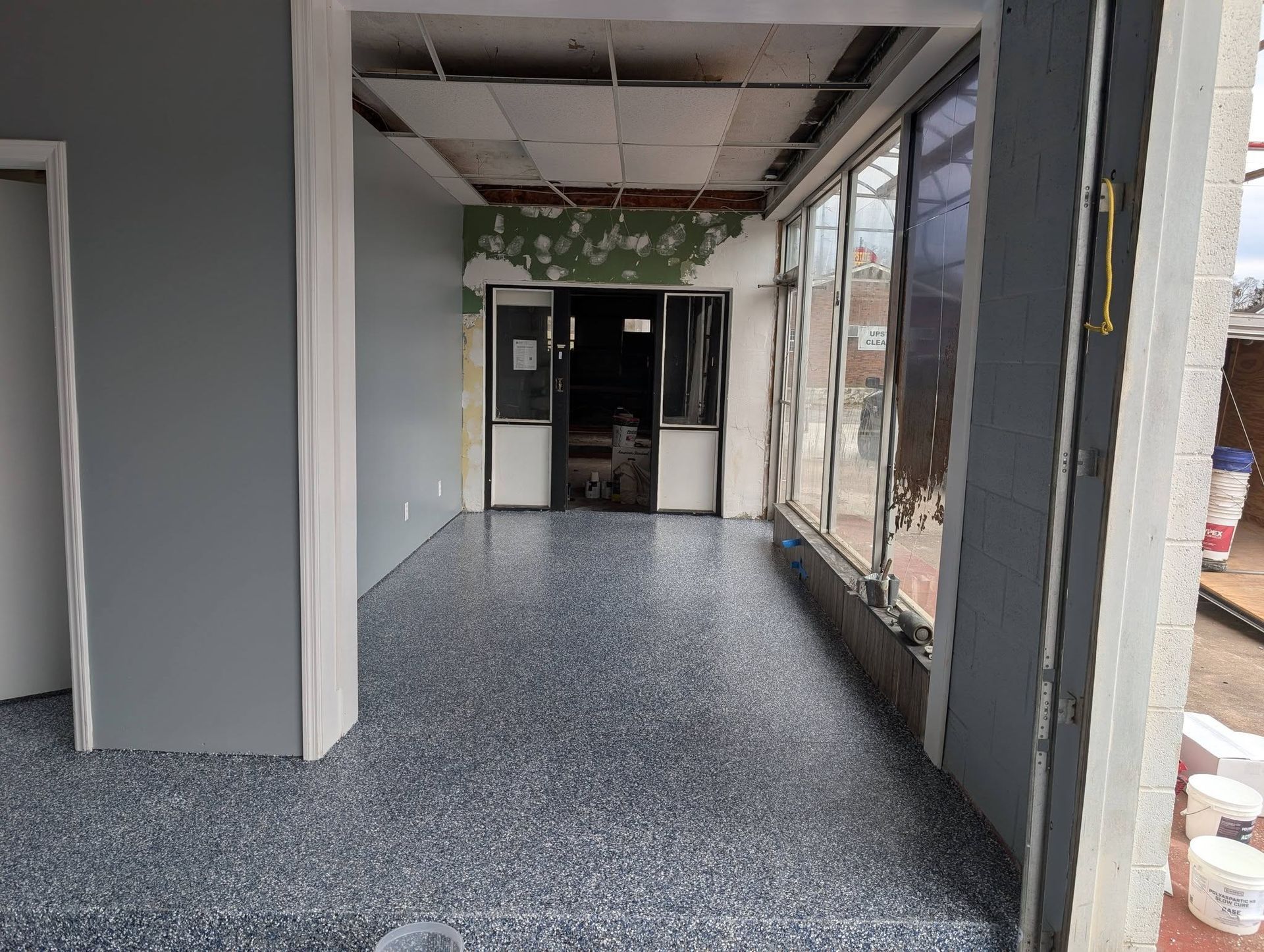 Empty storefront interior with gray speckled floor and large front windows.