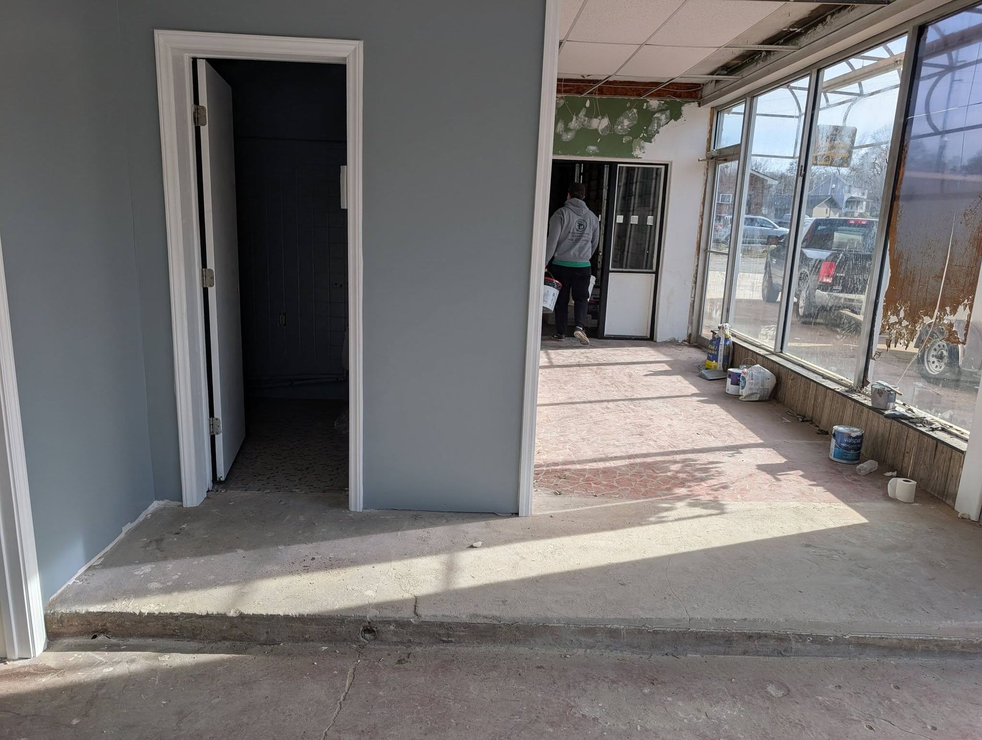 Empty storefront interior with gray walls, open door, and large windows overlooking a sidewalk.