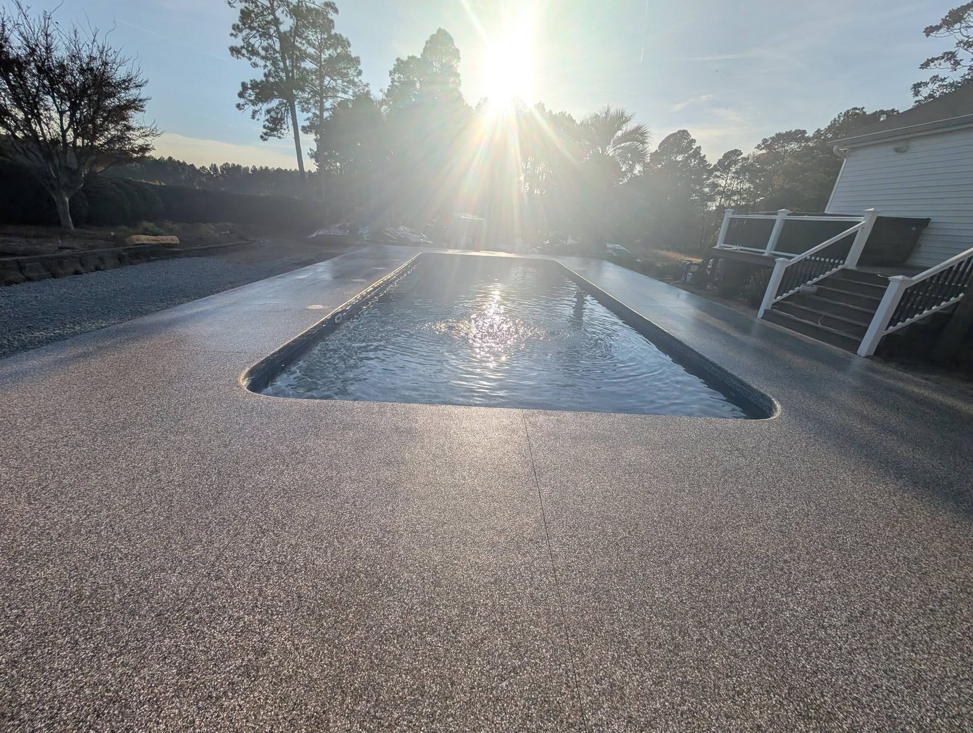 Sunlit backyard pool with clear water, paved deck, and lounge chairs at sunrise or sunset
