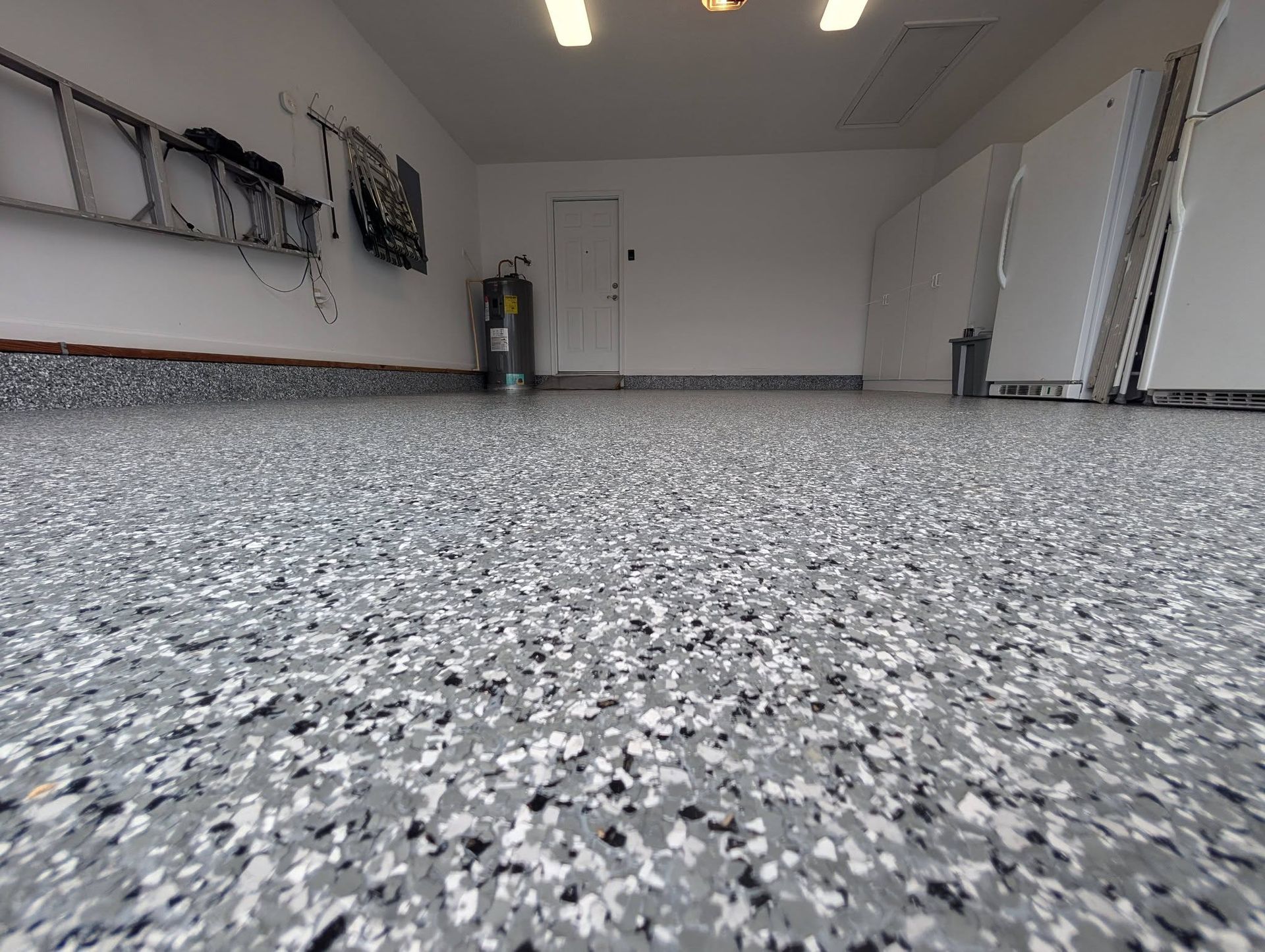 Empty garage with gray speckled floor and white walls, viewed from a low angle