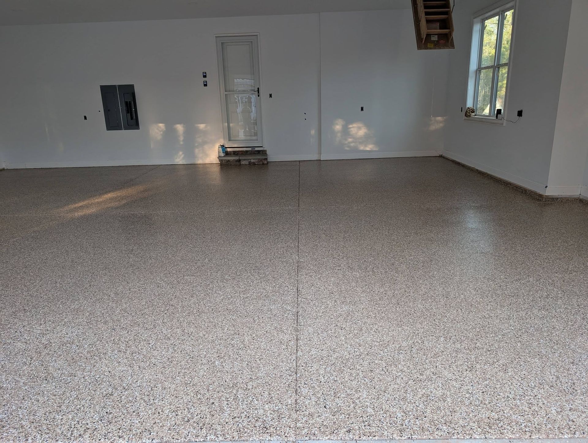 Empty room with white walls and speckled flooring, a window on the right, and a door at the back.