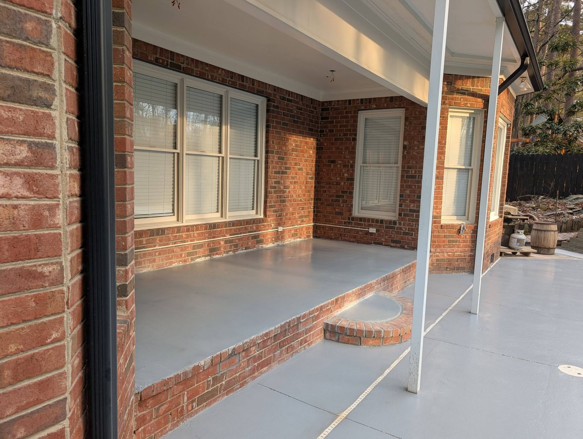 Brick house front porch with white posts, gray floor, and windows with blinds.