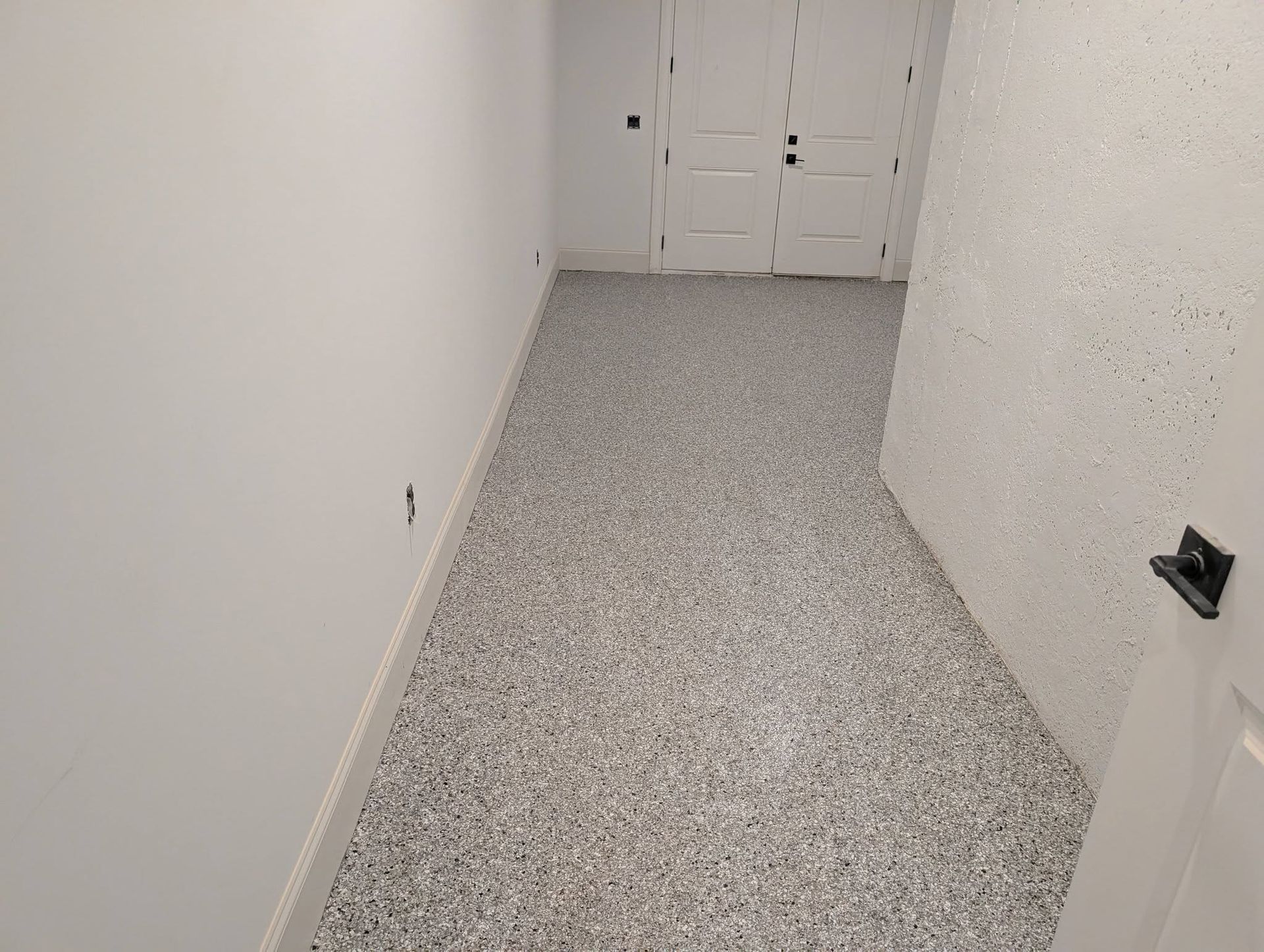 Narrow white hallway with speckled gray carpet leading to double doors at the end