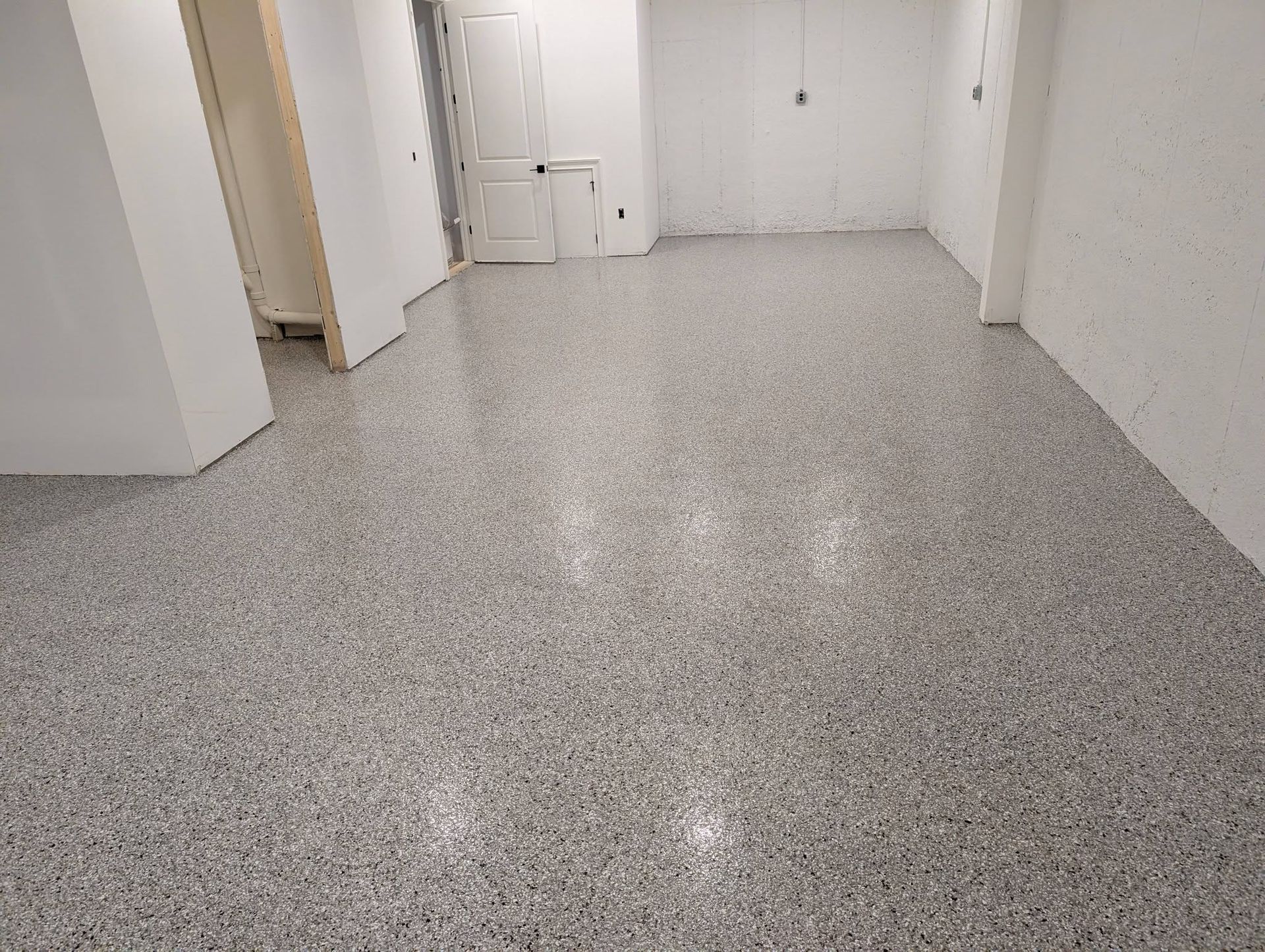 Empty white hallway with a speckled gray floor and open doorways