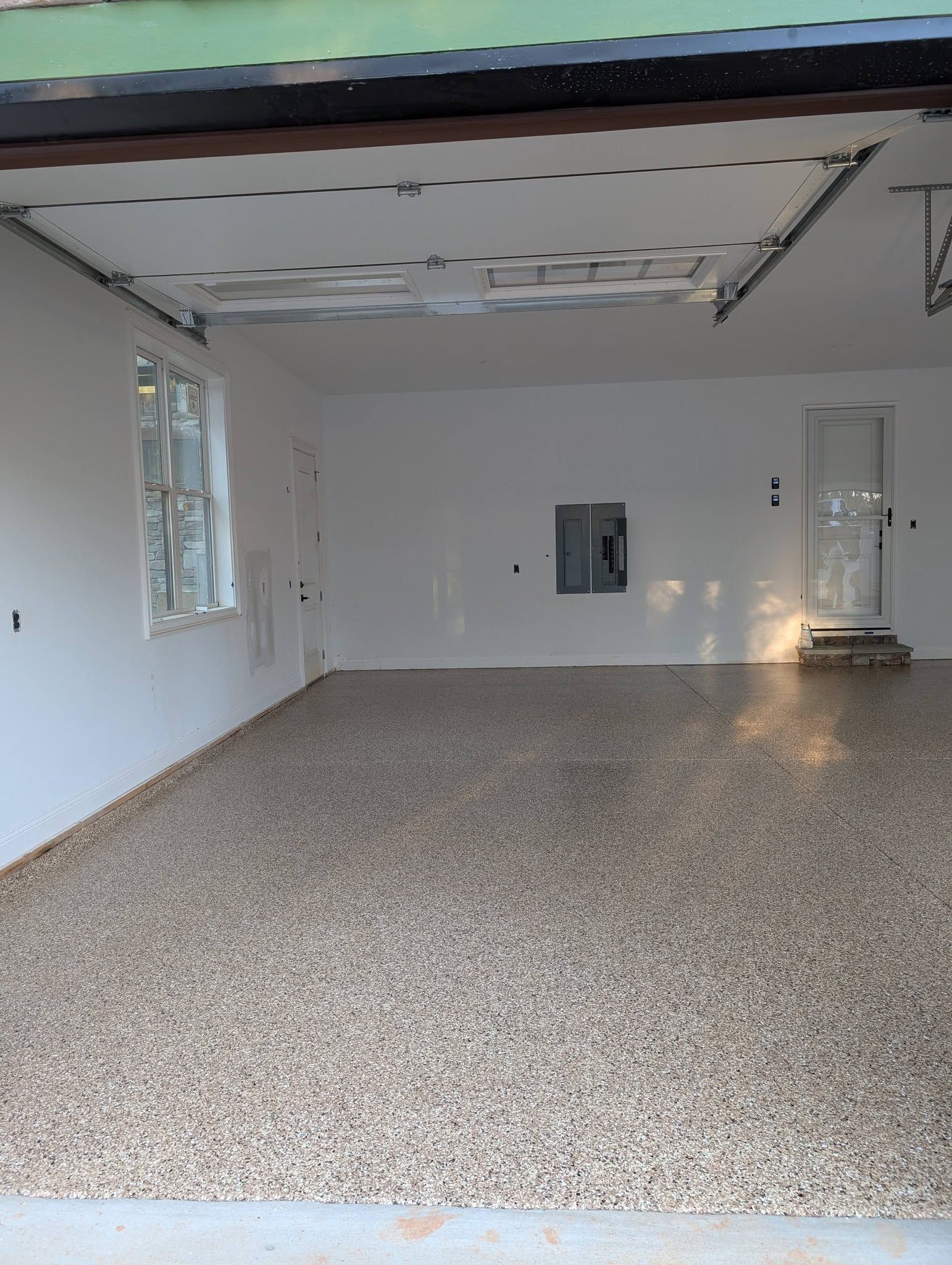 Empty garage interior with white walls, speckled floor, and open overhead door