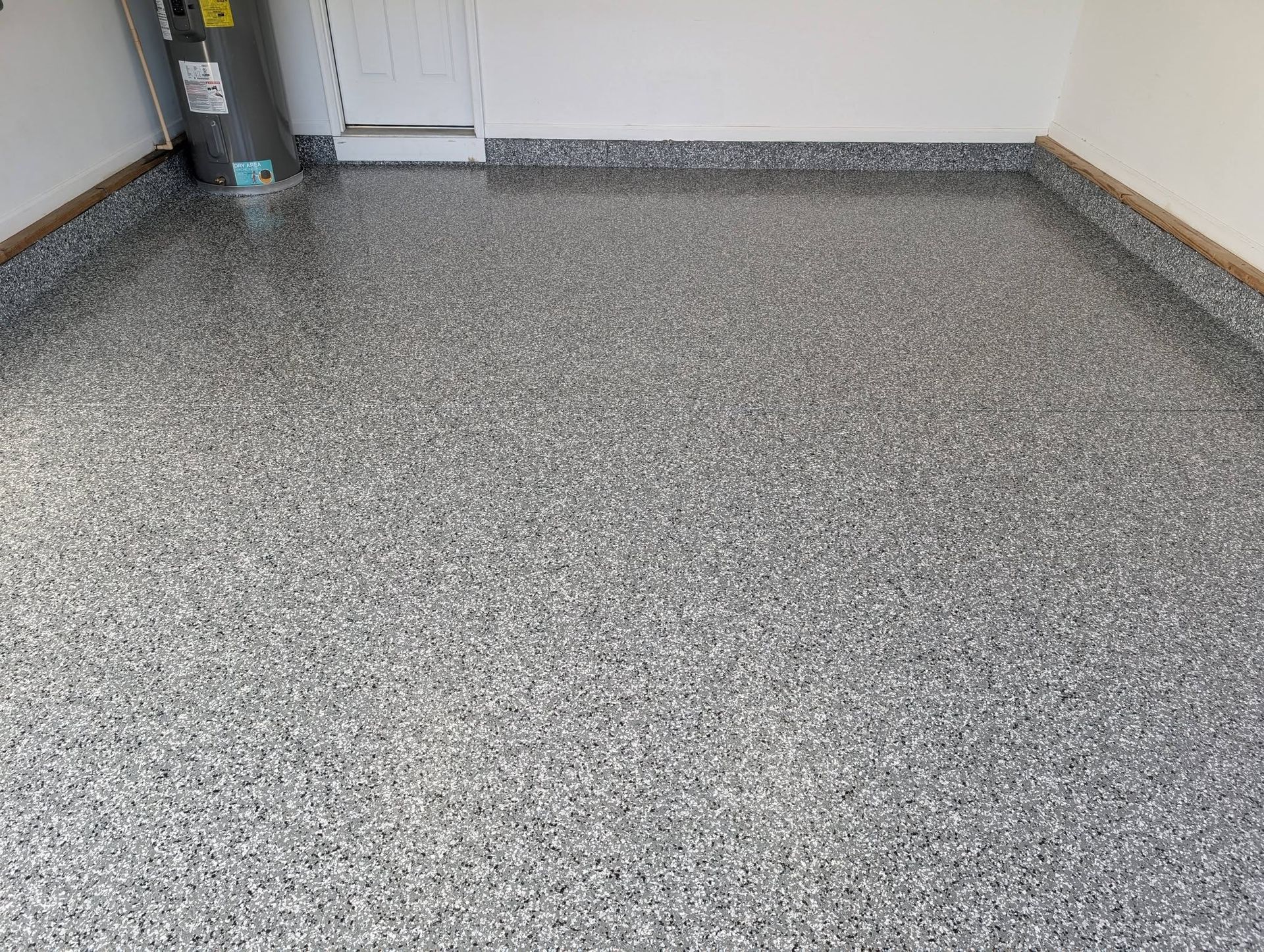 Empty room with speckled gray floor and white walls, showing a corner and baseboards.