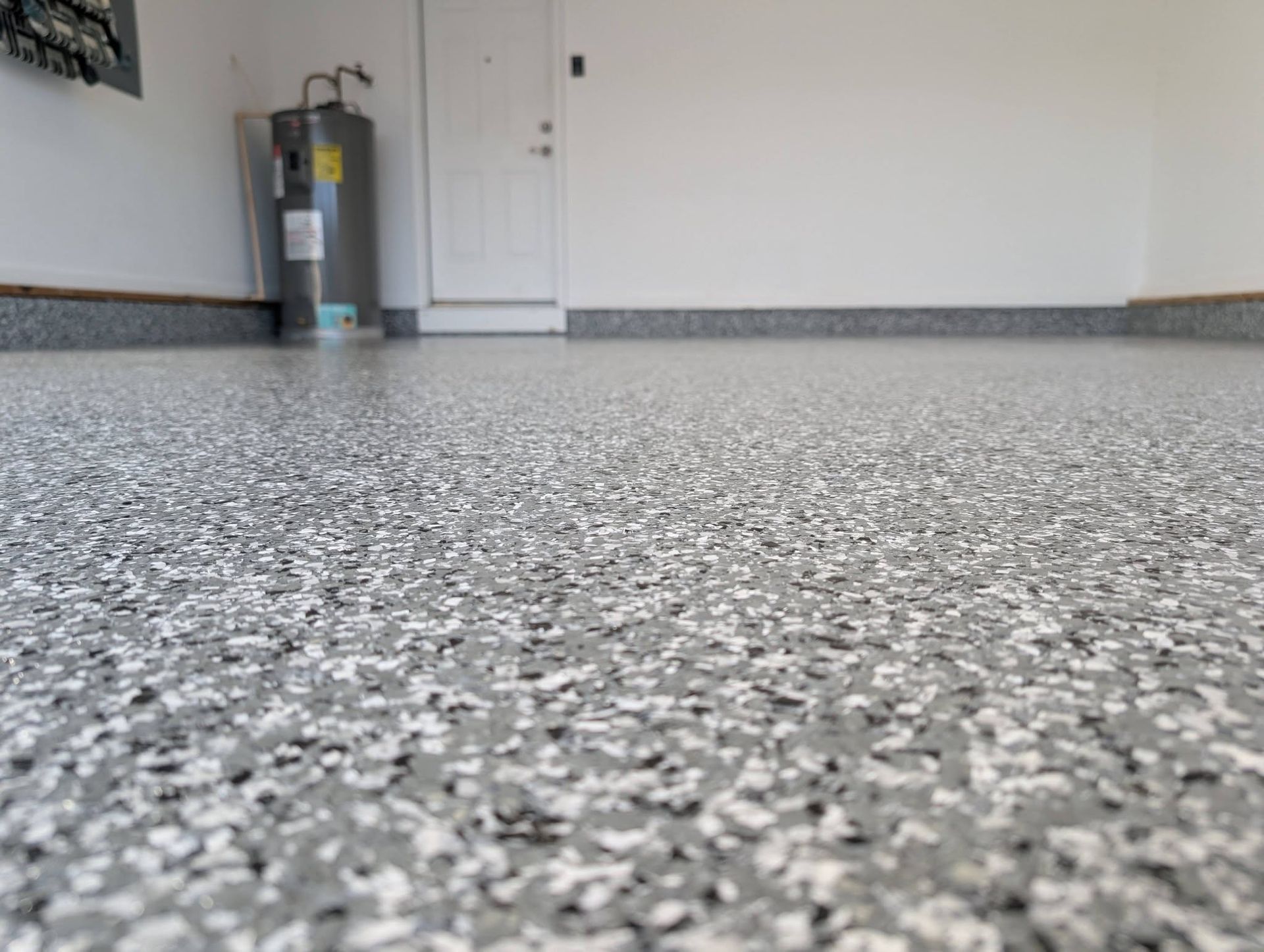 Empty speckled garage floor with white walls and a utility tank in the background