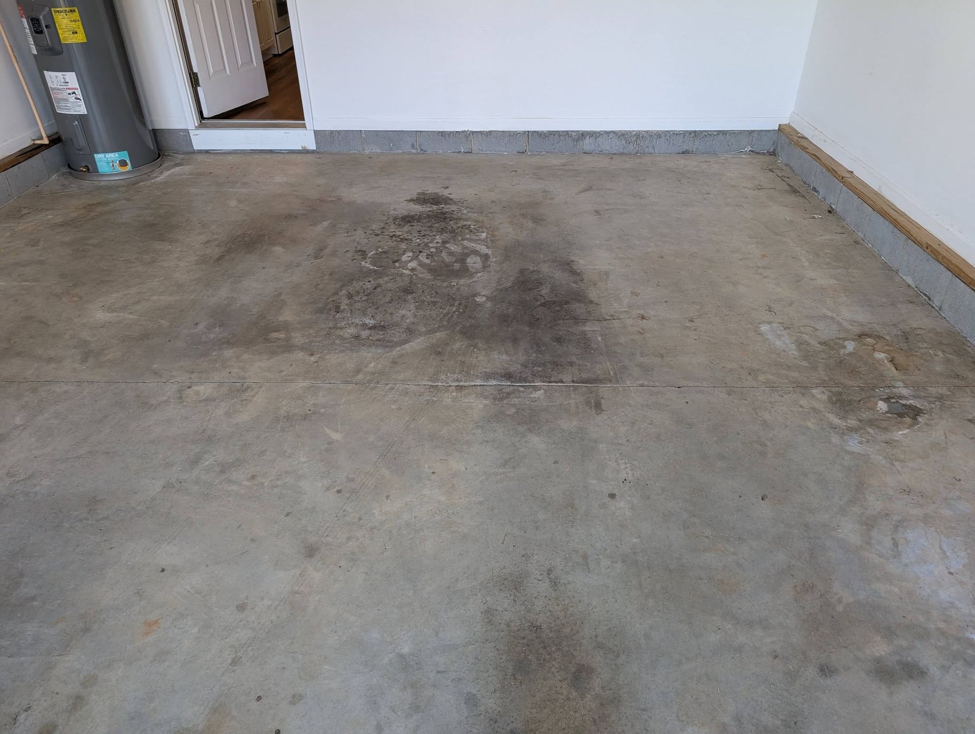 Empty garage with stained concrete floor and white walls, viewed from the open doorway