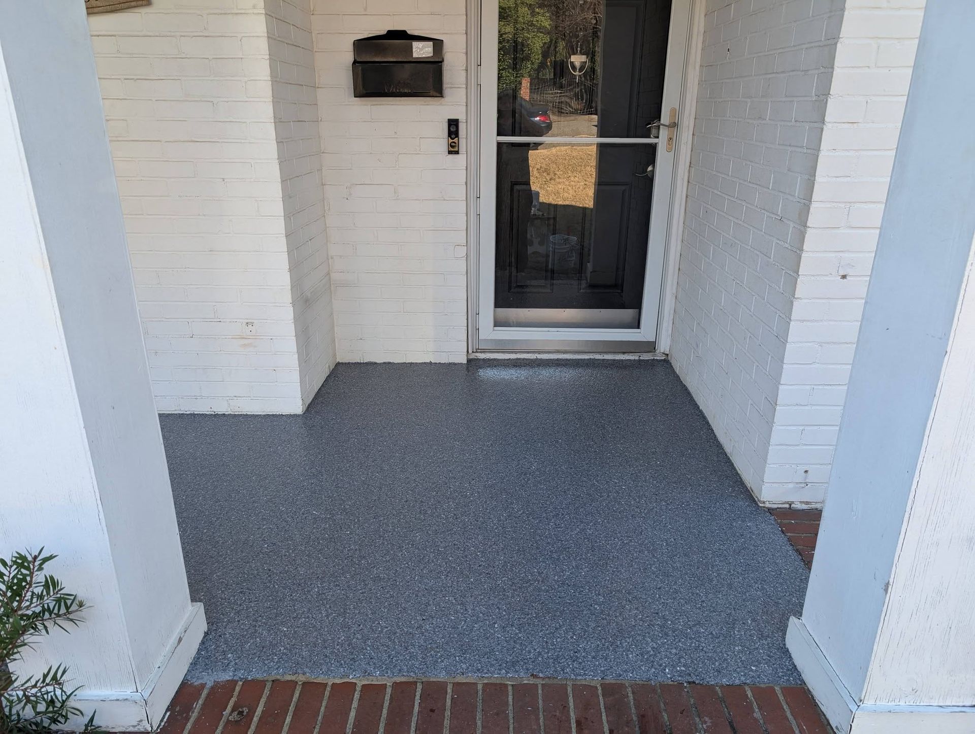 Front porch with white brick walls, gray floor, and a glass front door.