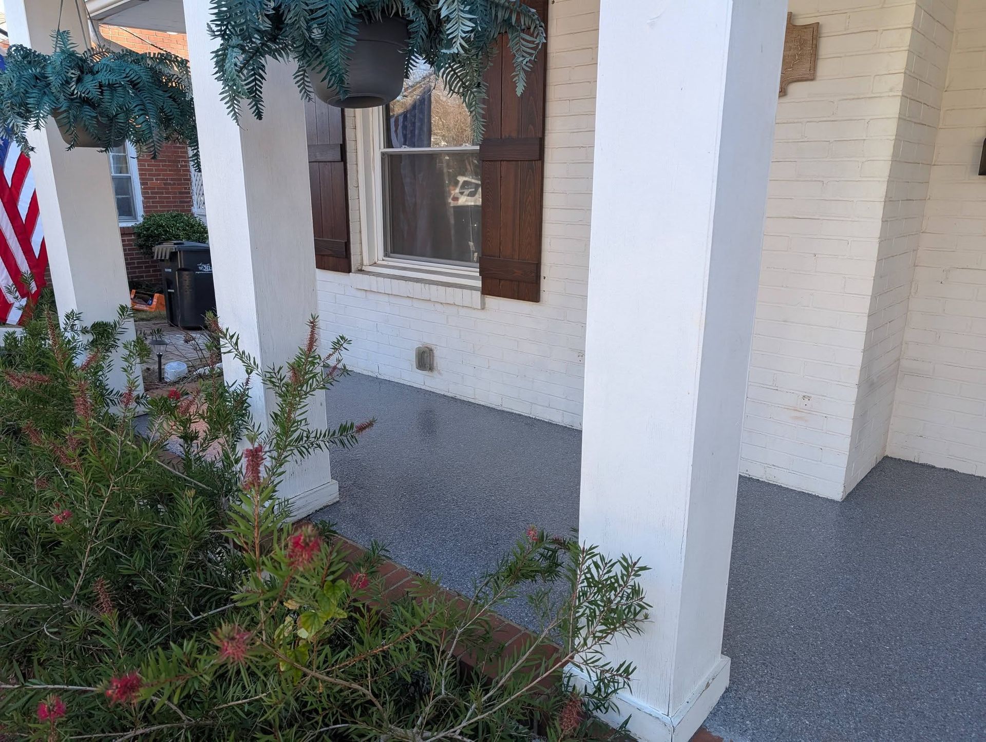 Front porch with white columns, brown shutters, hanging greenery, and red flowers by the walkway