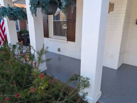 Front porch with white columns, brick wall, window, hanging greenery, and an American flag.