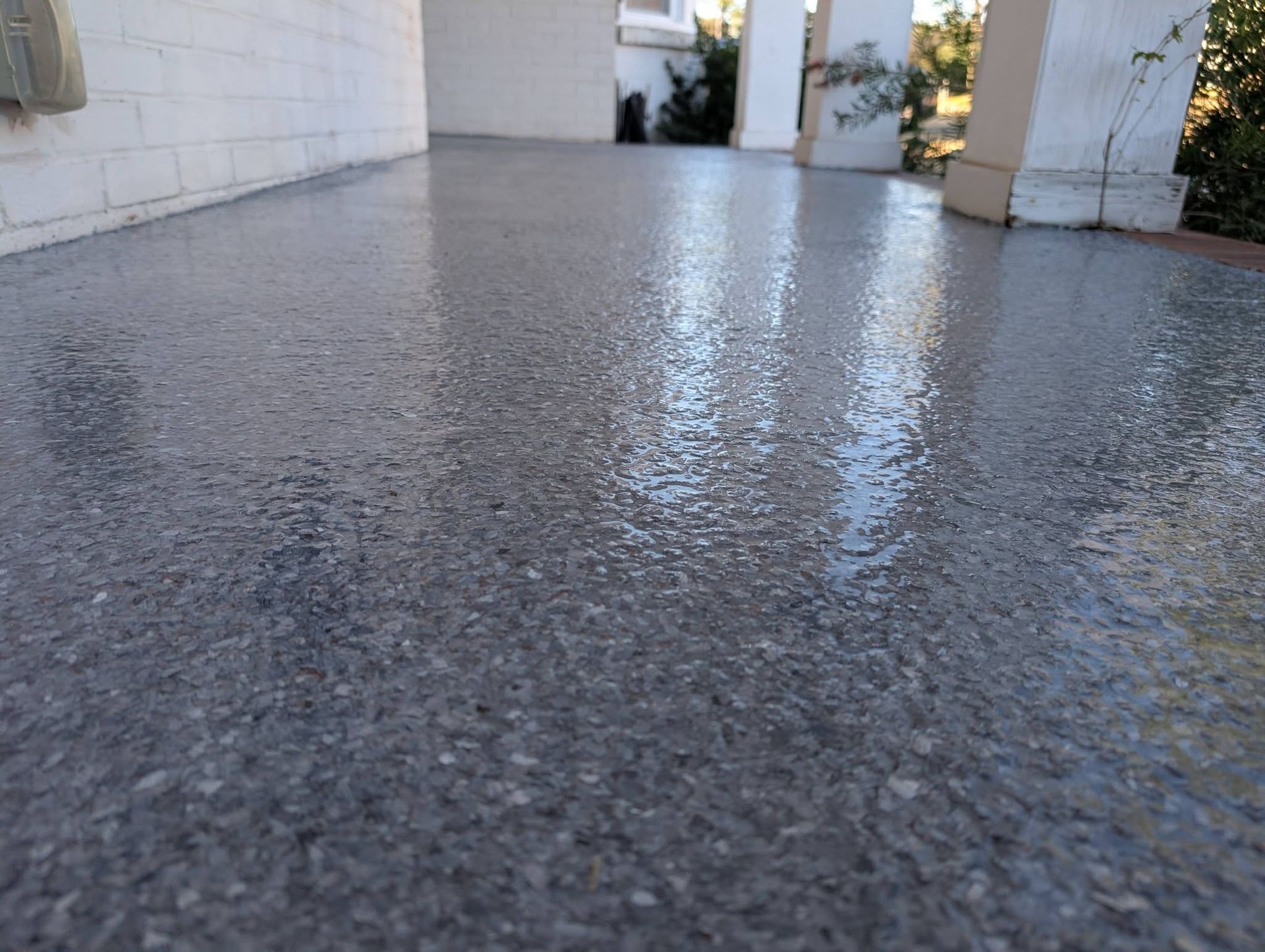 Wet concrete patio reflecting light beside a house and columns