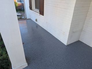 Narrow outdoor walkway with white stucco walls and gray textured floor, leading to a small yard.