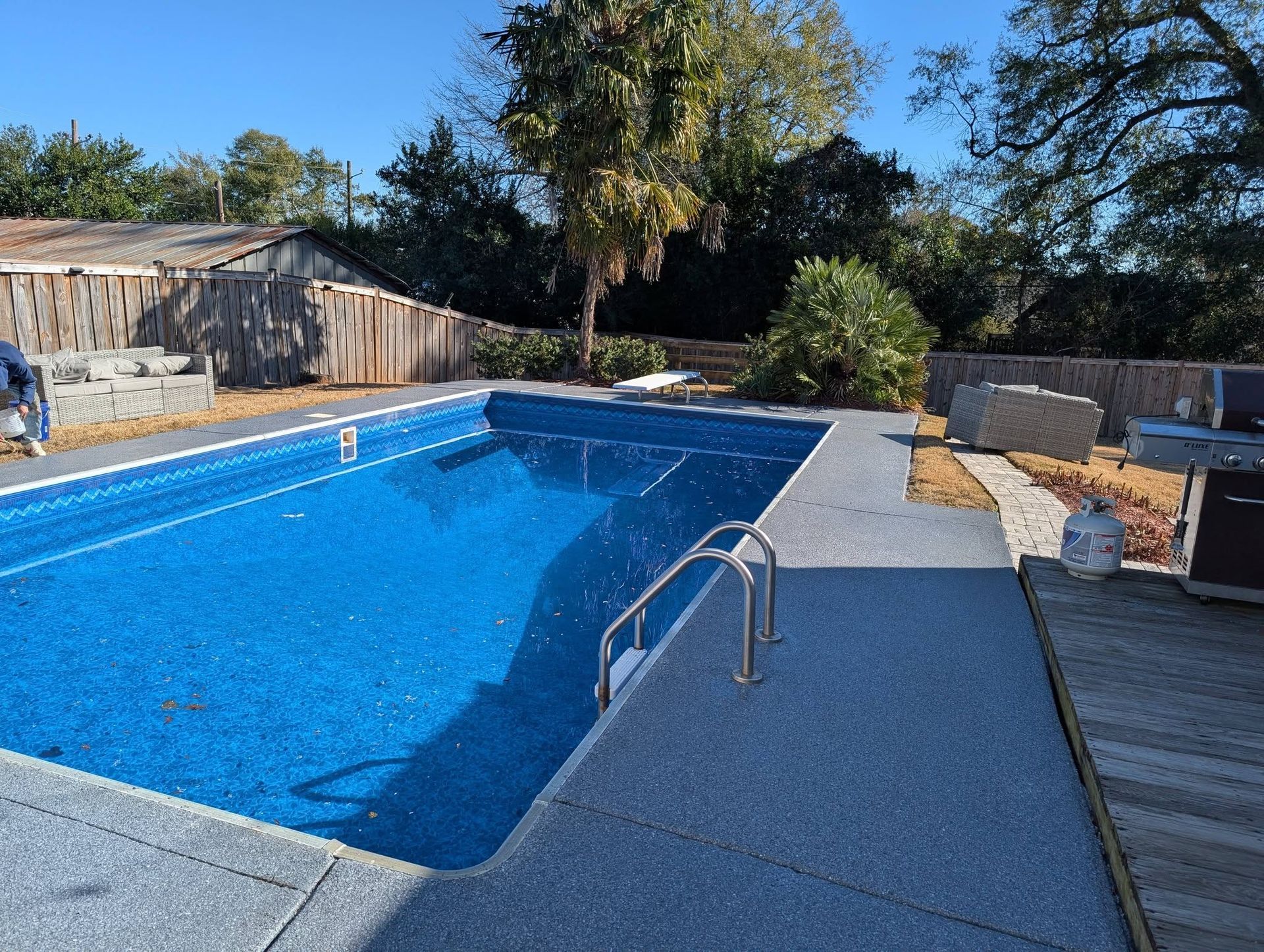 Backyard swimming pool with blue water, metal ladder, and surrounding patio in sunlight