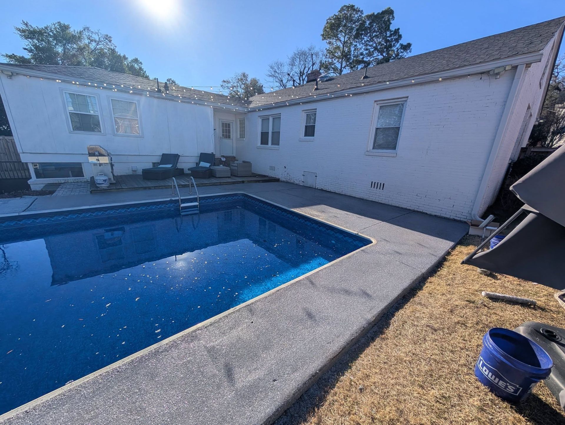 Backyard pool beside a white house under bright sunlight