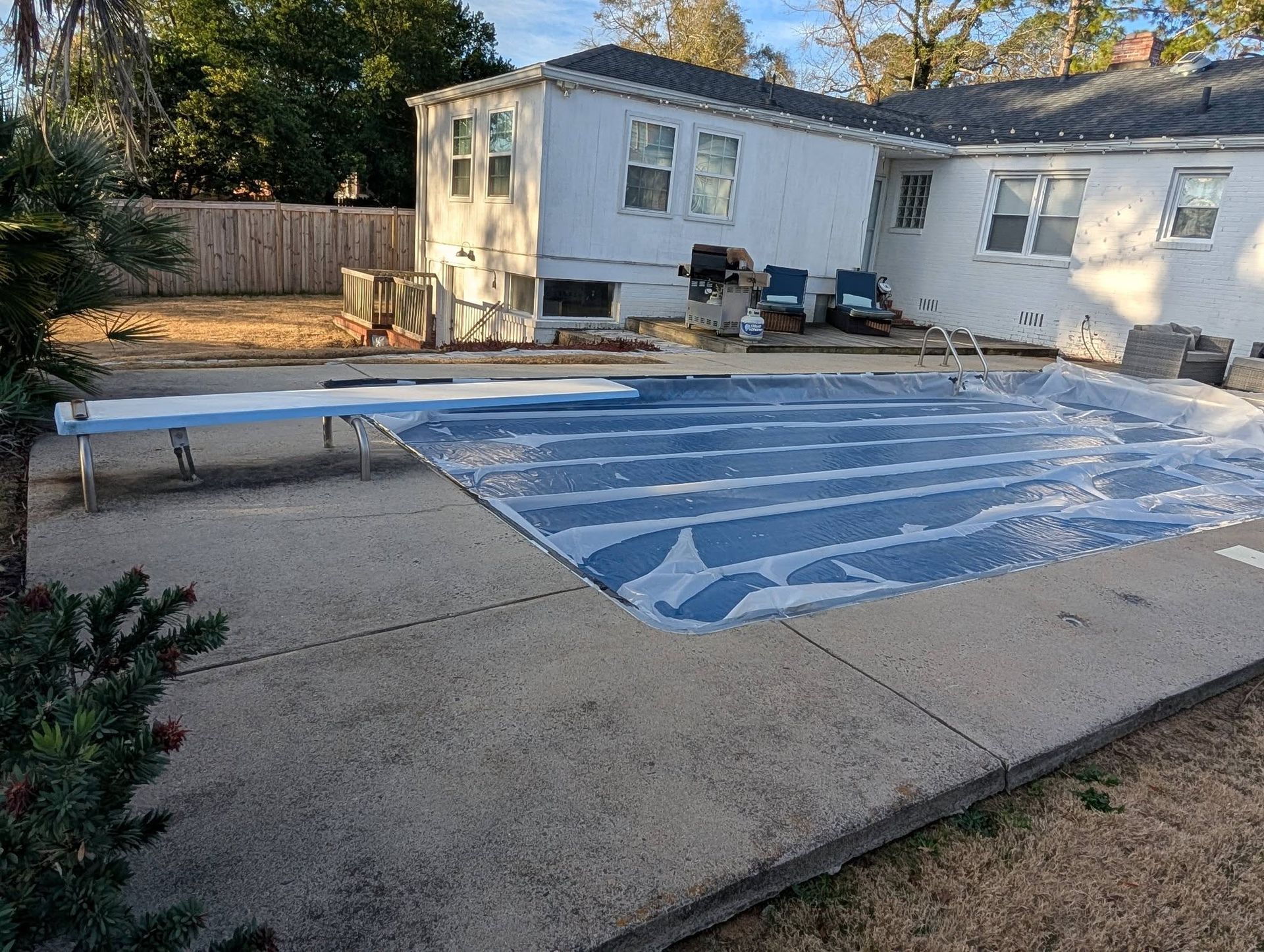 Backyard pool under construction with blue liner, concrete deck, and a white house in the background