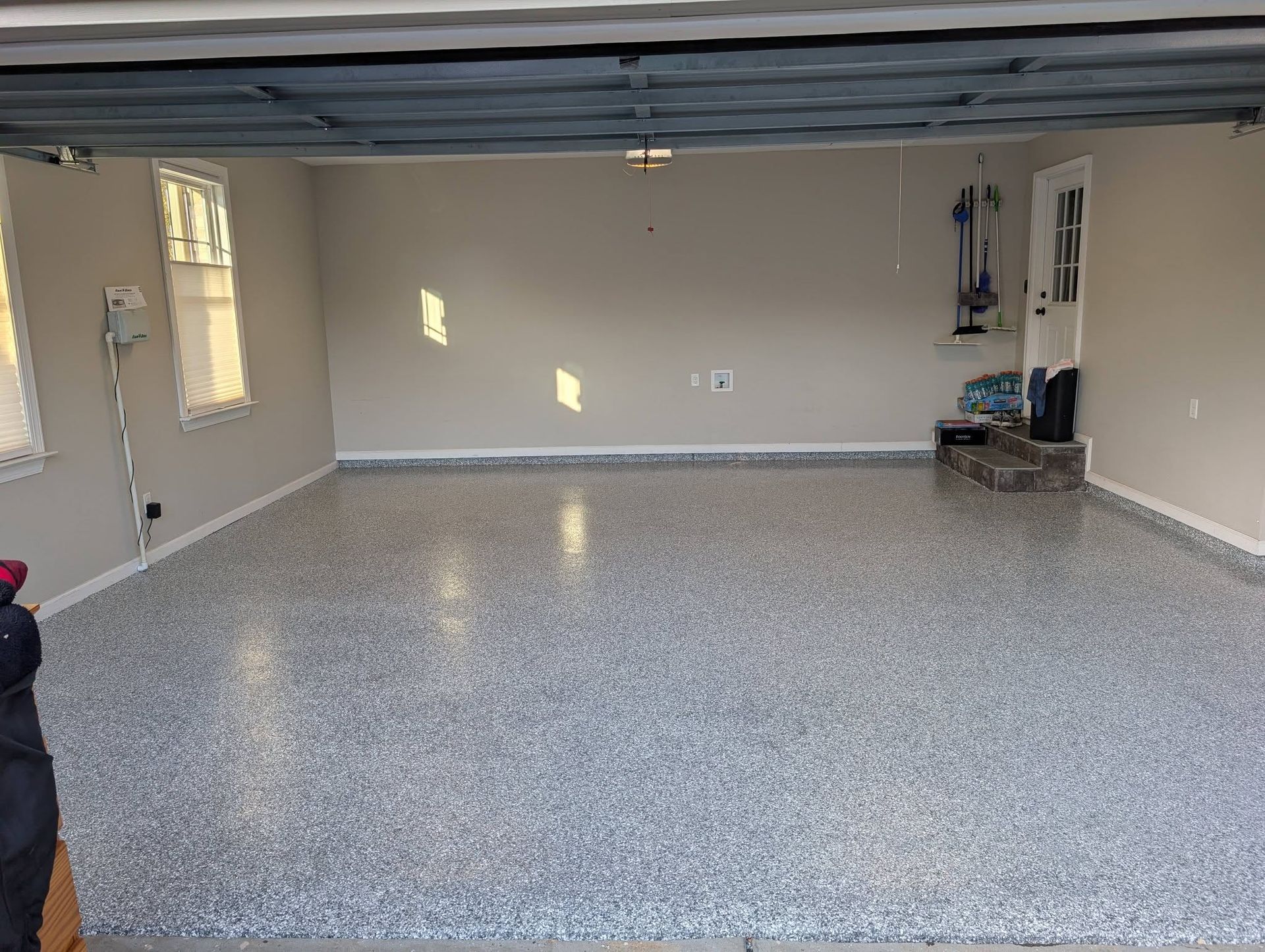Empty garage with speckled epoxy floor and open door, lit by sunlight from side windows