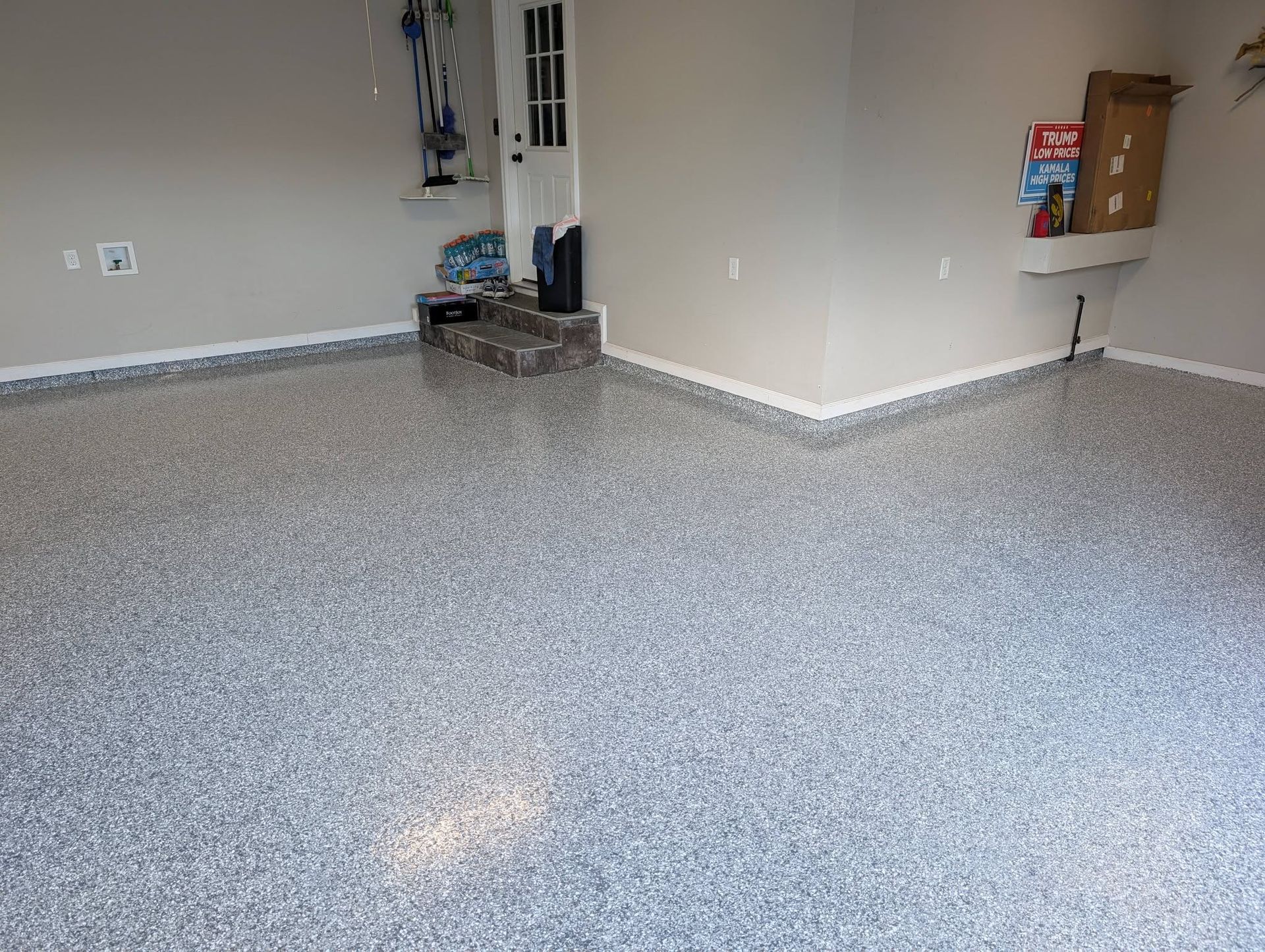 Empty garage with speckled epoxy floor, beige walls, and a small storage area in the corner