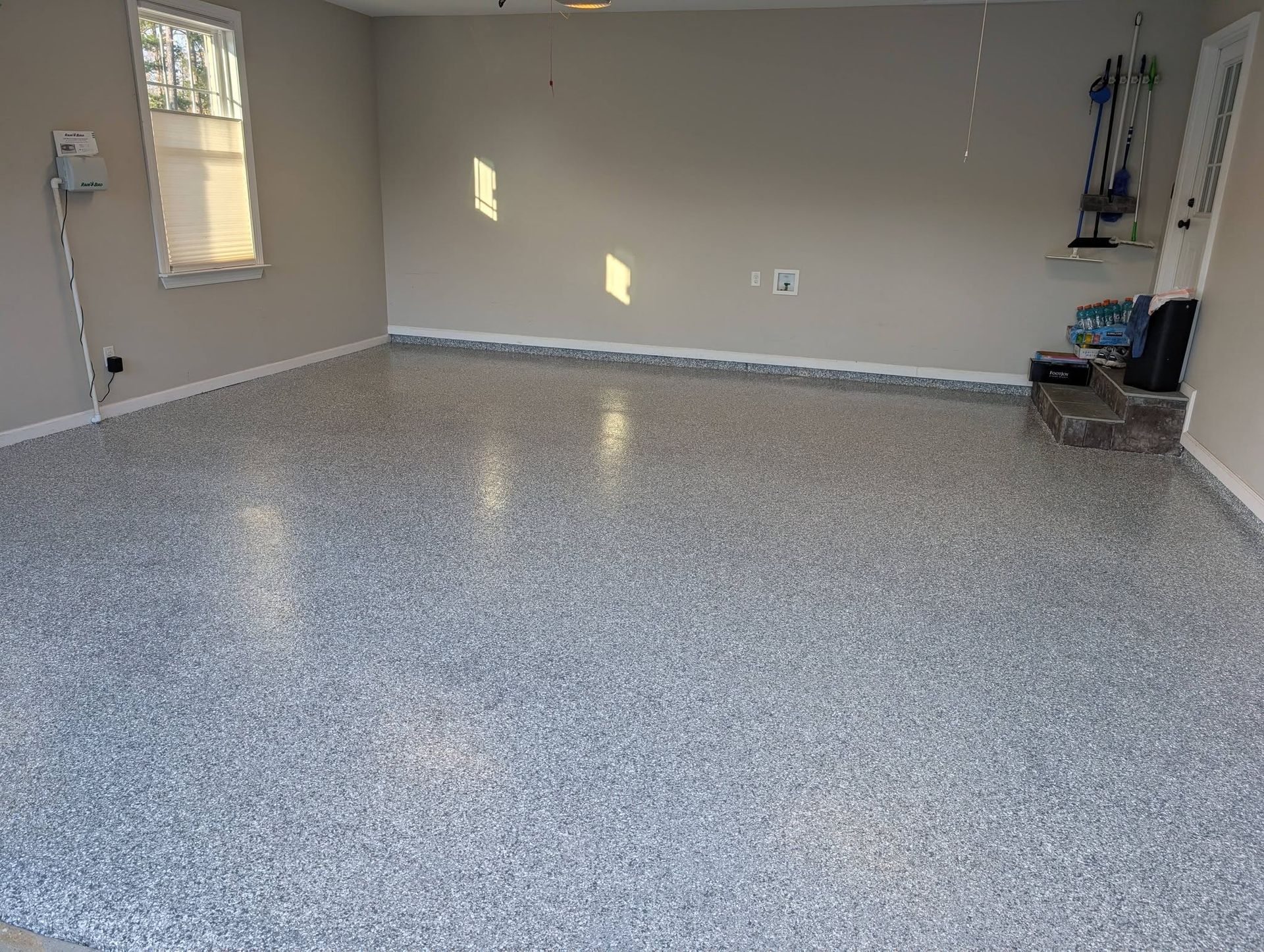 Empty garage with speckled epoxy floor and a closed door at the back wall