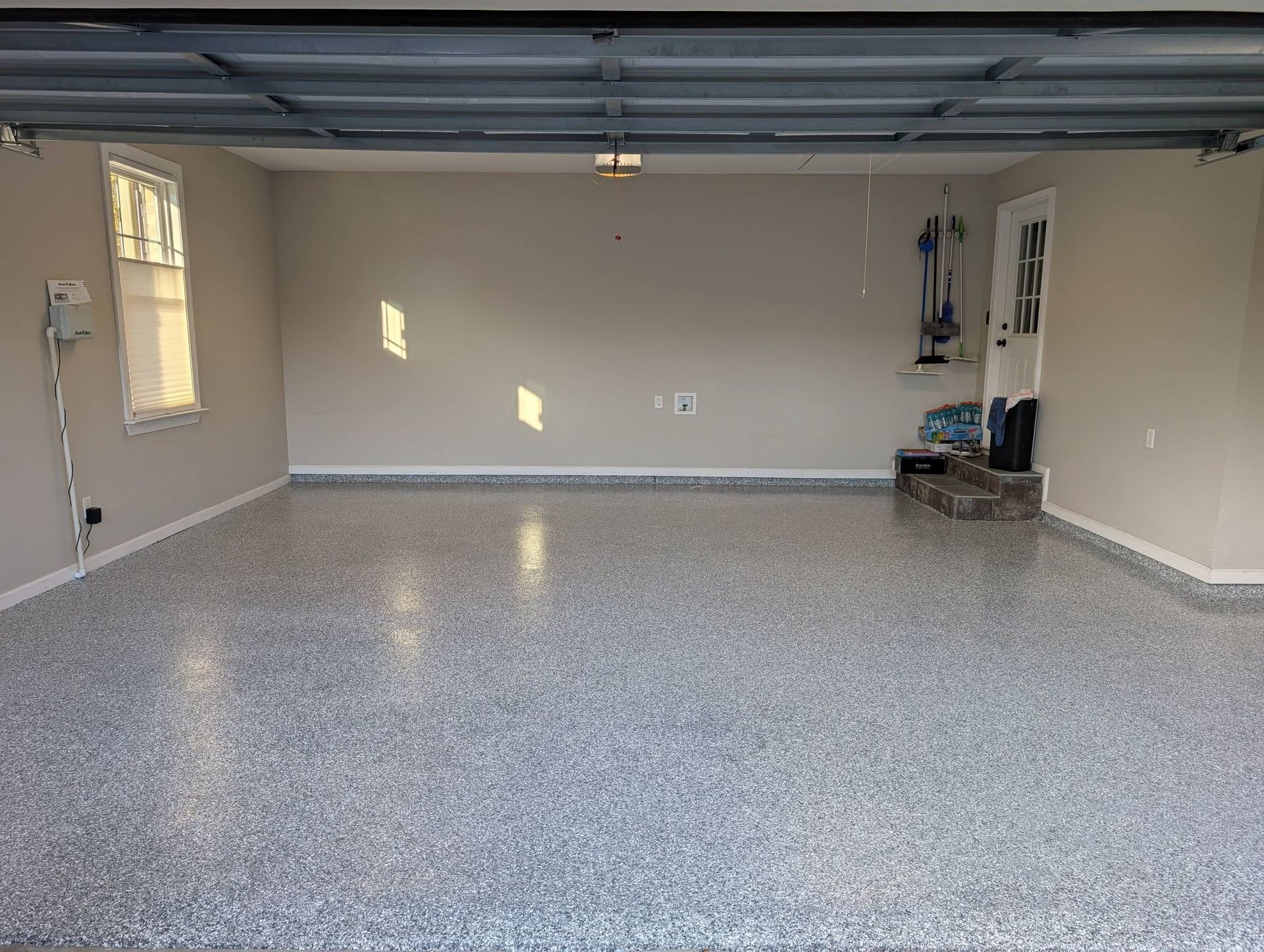 Empty garage with speckled epoxy floor, beige walls, small window, and overhead door rails.