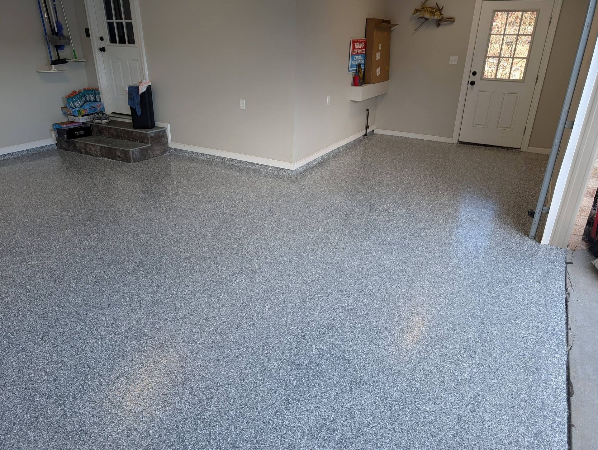 Empty garage with speckled epoxy floor, white walls, utility sink, and door to the outside.