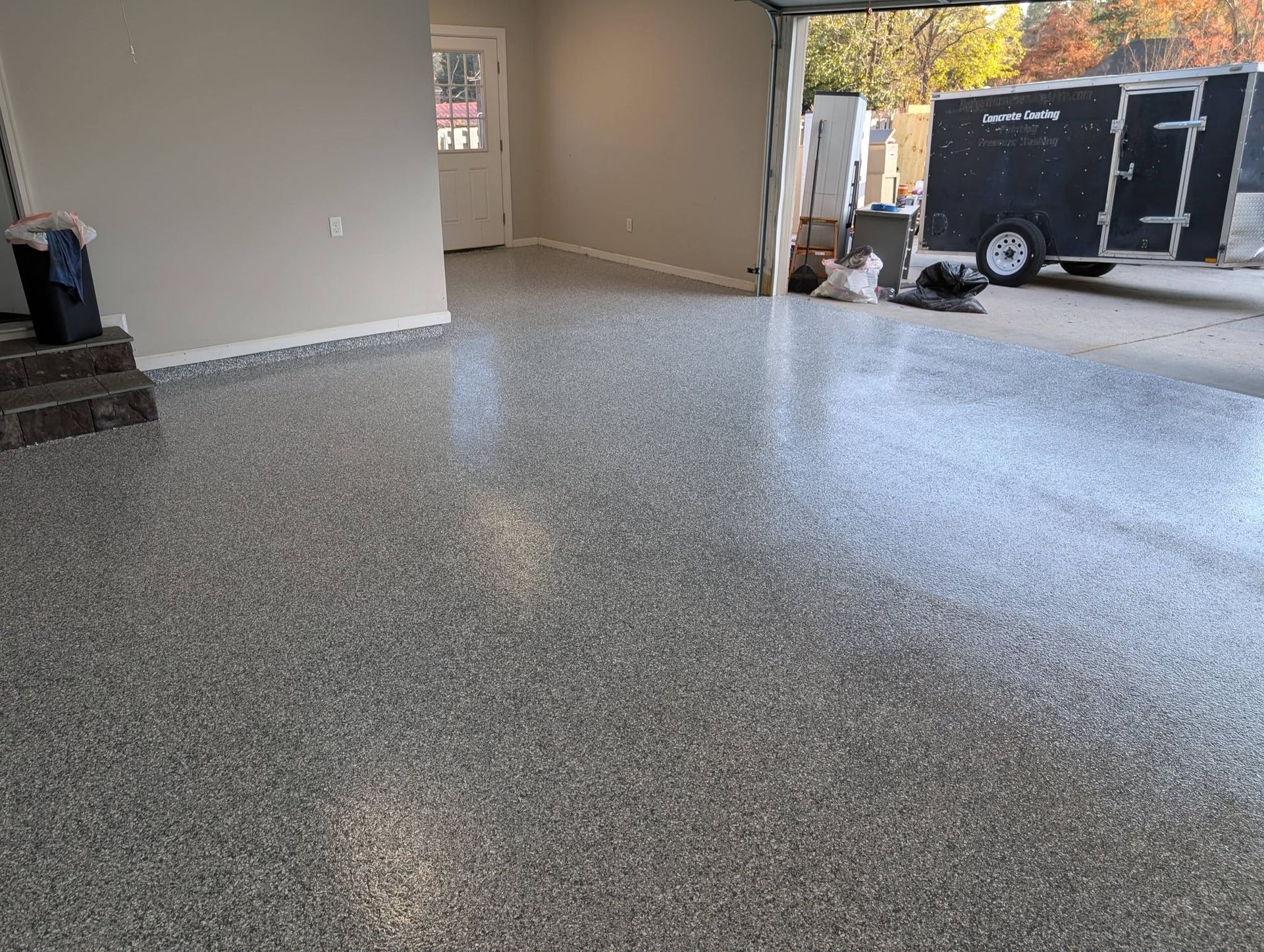 Empty garage with speckled epoxy floor and an open doorway to a trailer outside