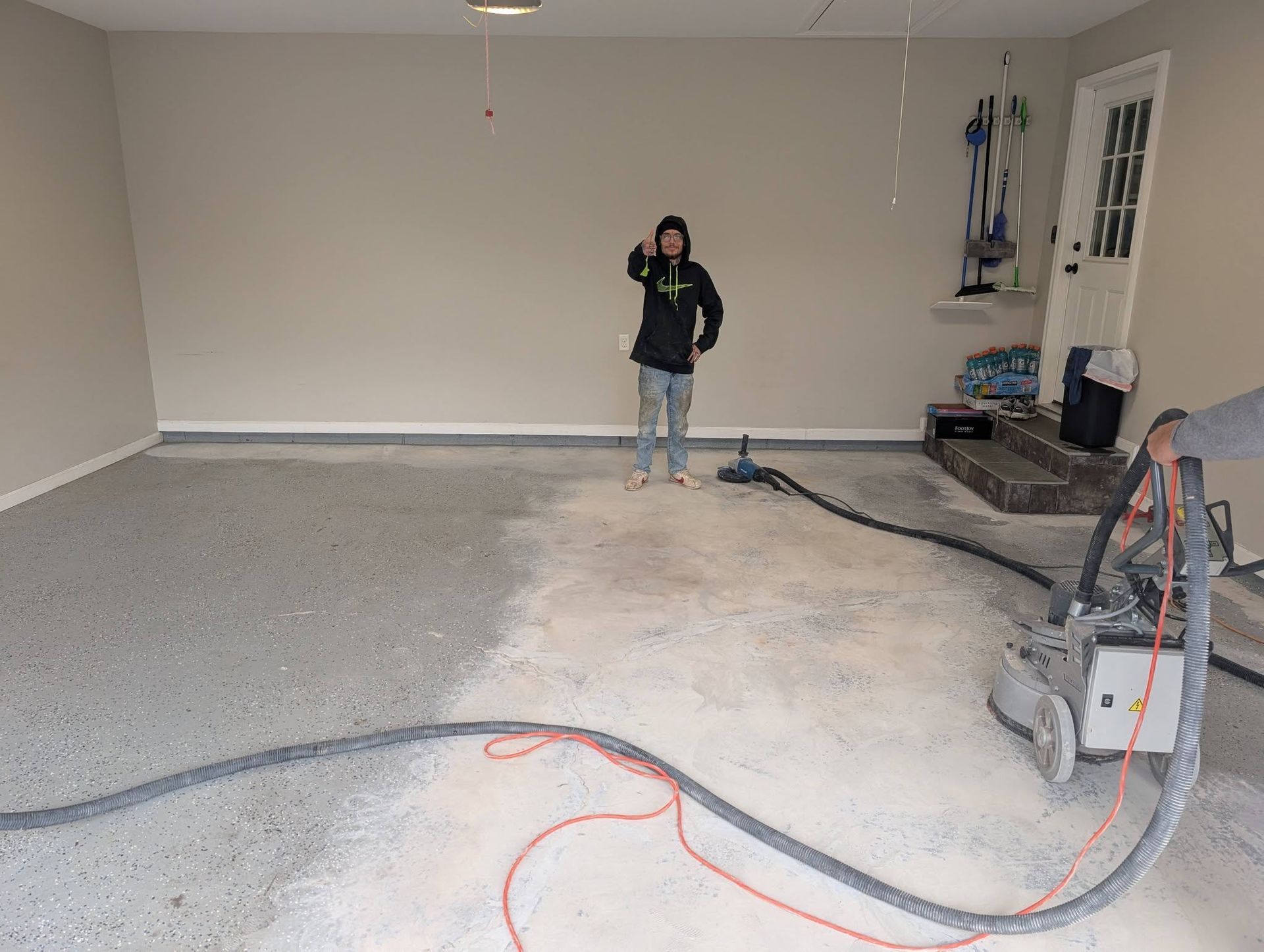 Person standing in a mostly empty garage with a concrete floor and tools along the right wall.