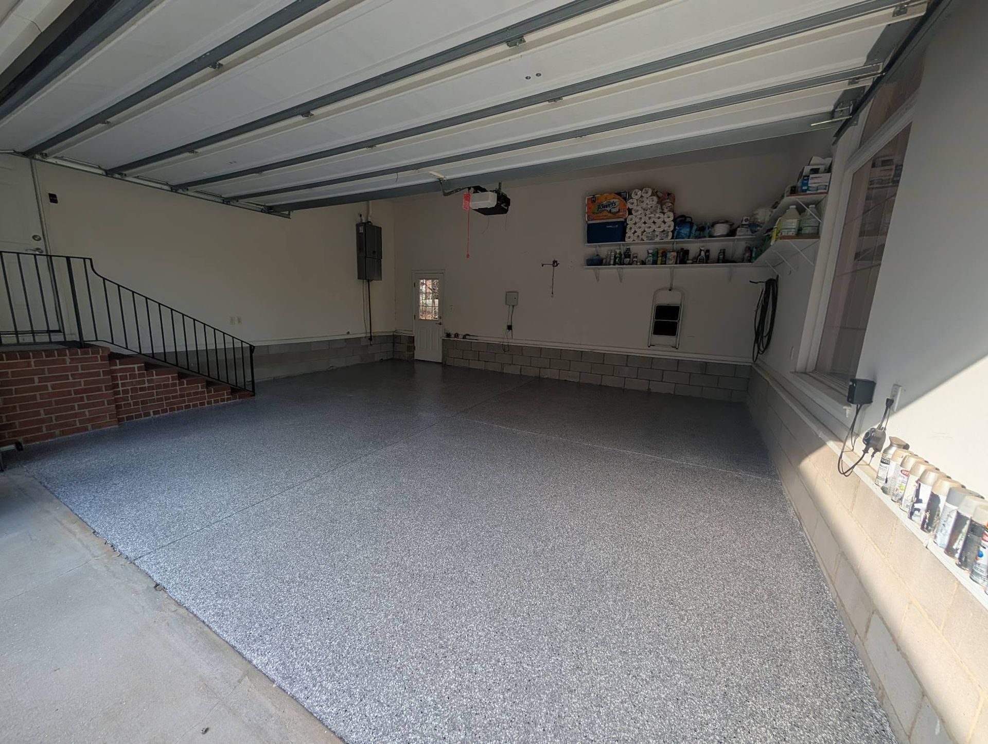 Empty garage with gray speckled floor, open interior, and shelves along the back wall.