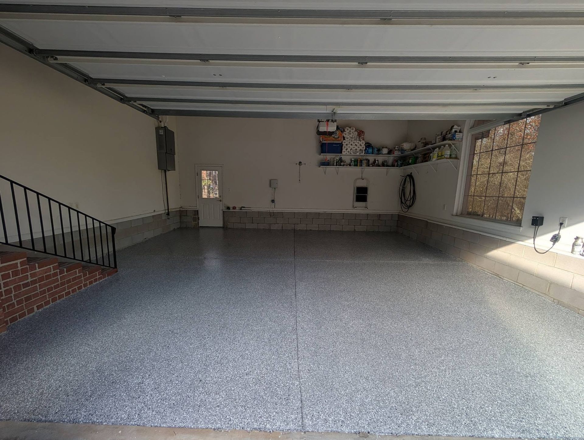 Empty garage with speckled gray floor, exposed beams, and a staircase on the left.