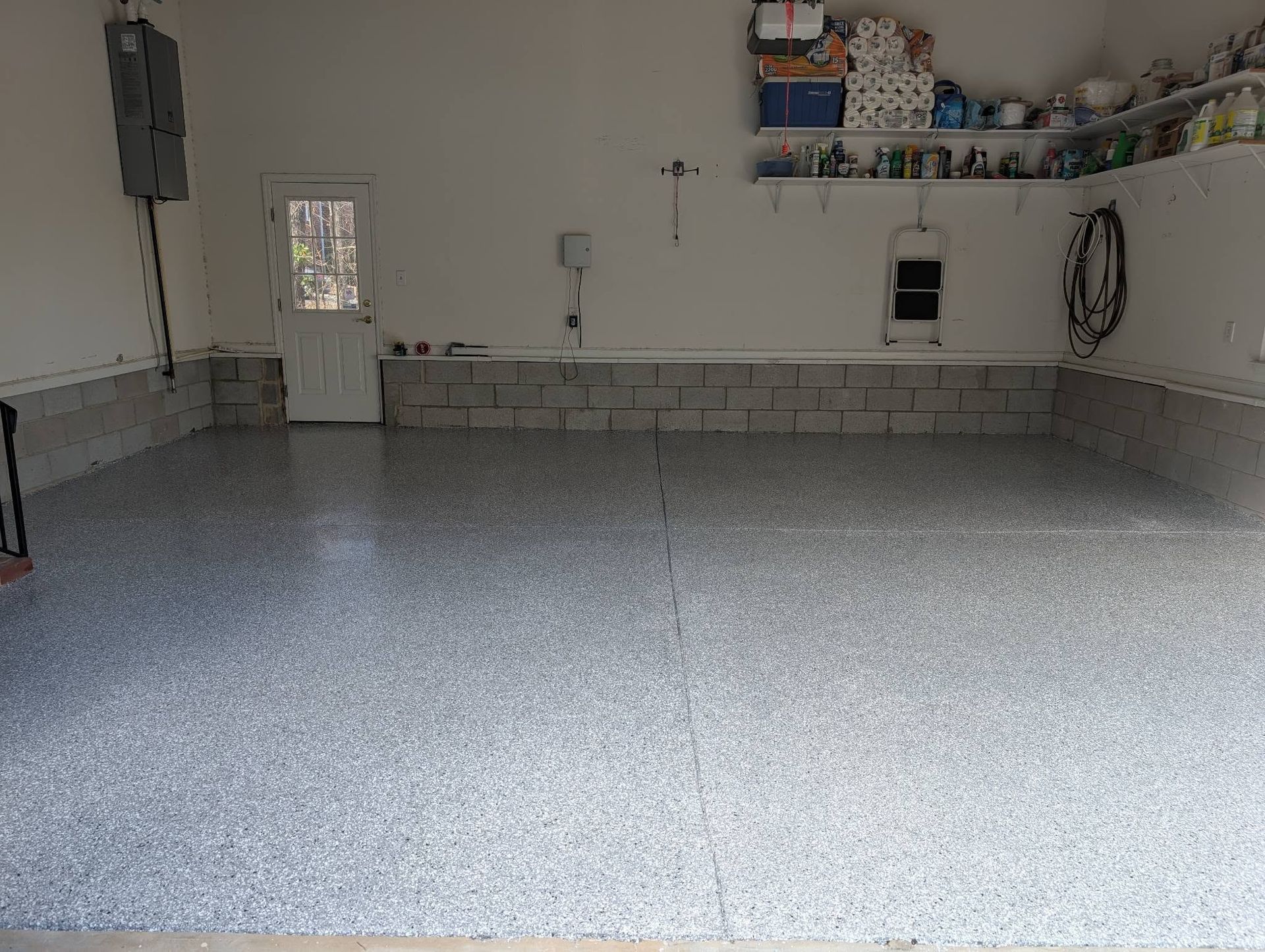 Empty garage with gray speckled floor, white walls, storage shelves, and a side door.