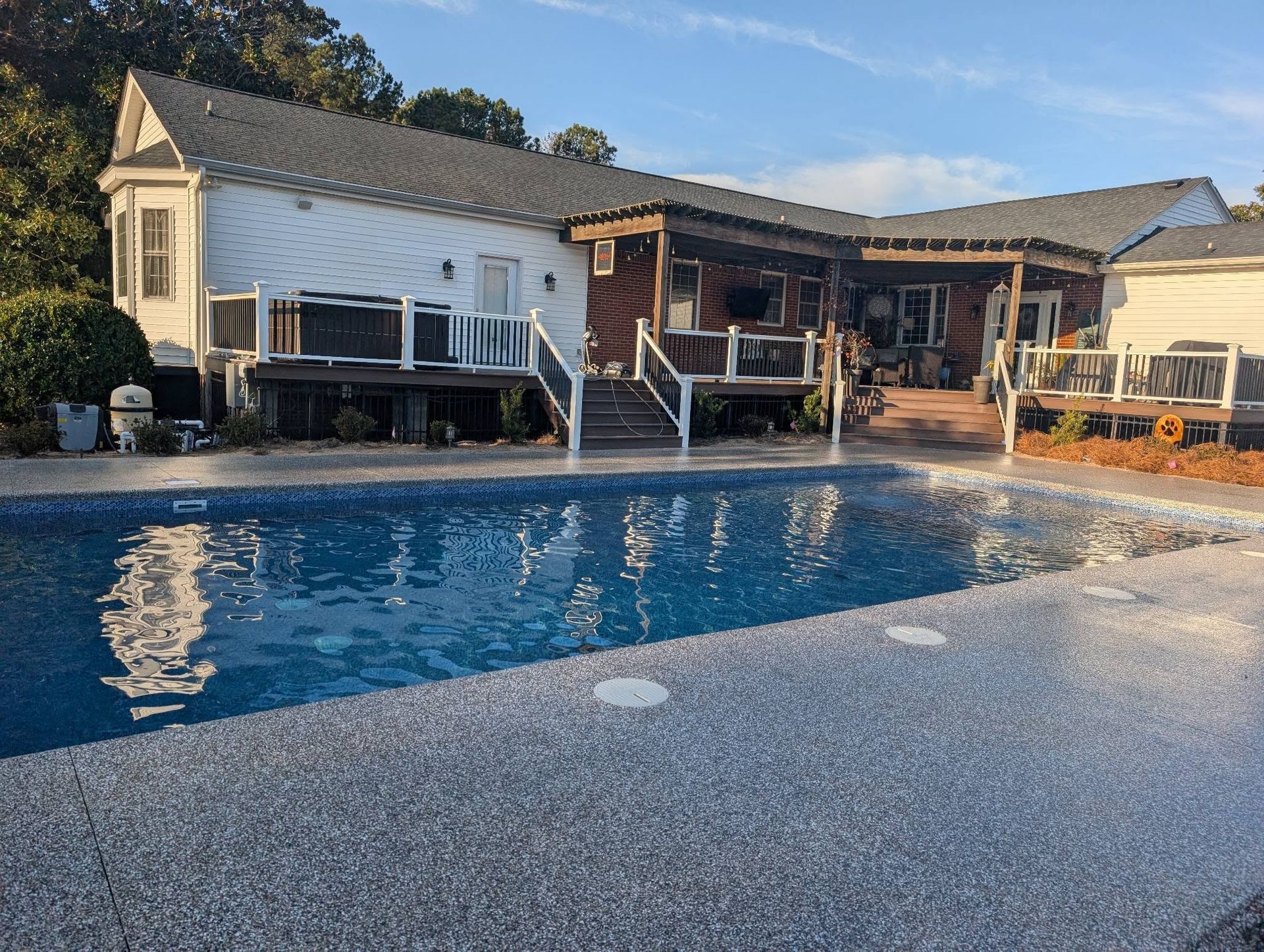 Backyard pool with a white house and covered patio in the background at sunset