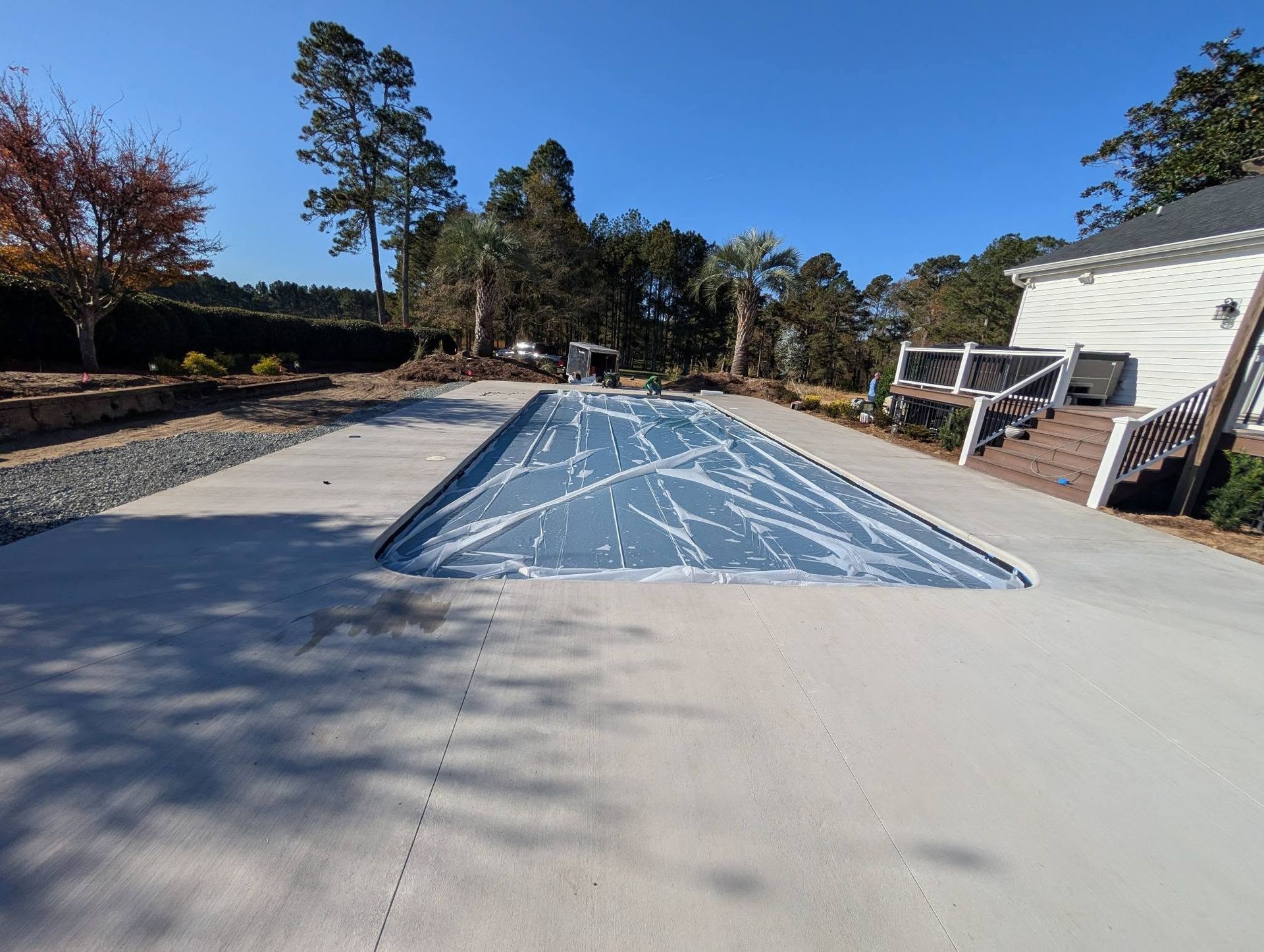 Empty outdoor swimming pool with blue liner in a sunny yard, surrounded by trees and a house.