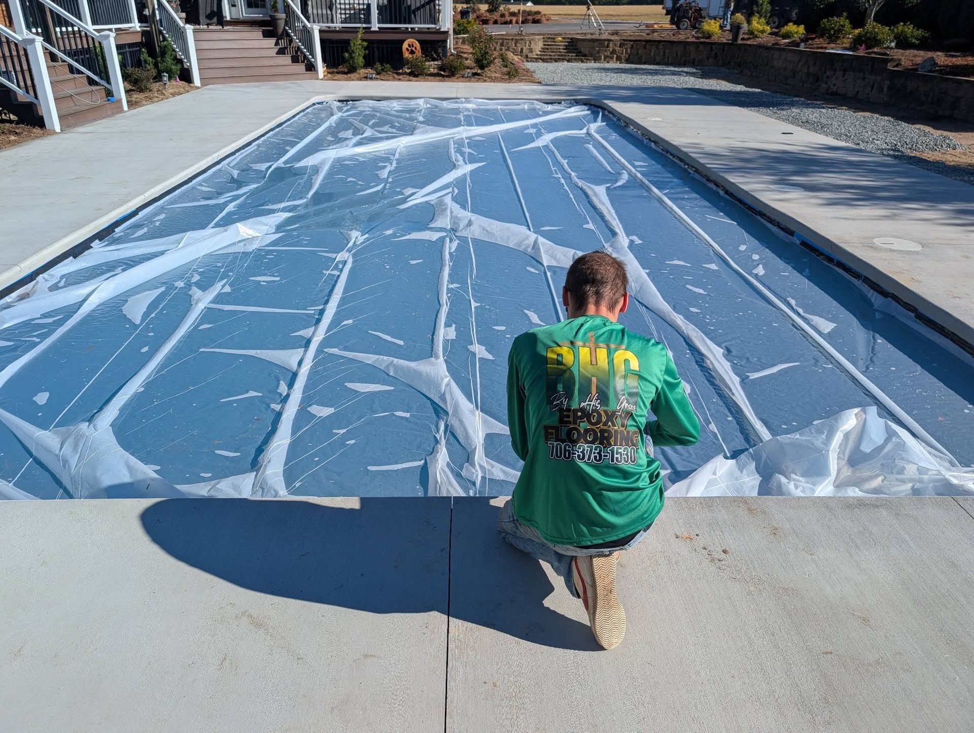 Person kneeling by a blue outdoor court covered in white markings, with houses and stairs in the background