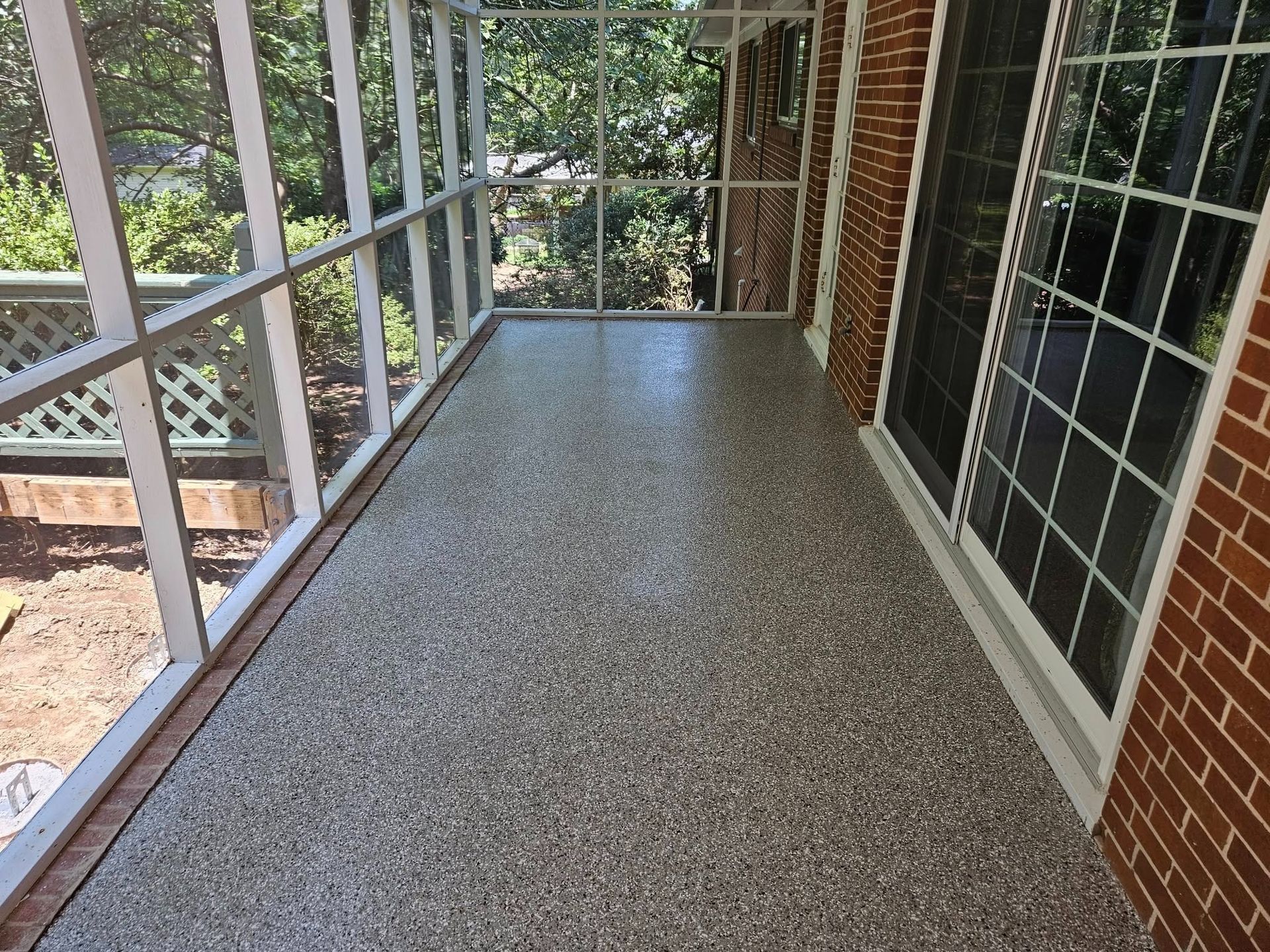 Covered porch with speckled floor, screened railing, and brick wall beside large windows