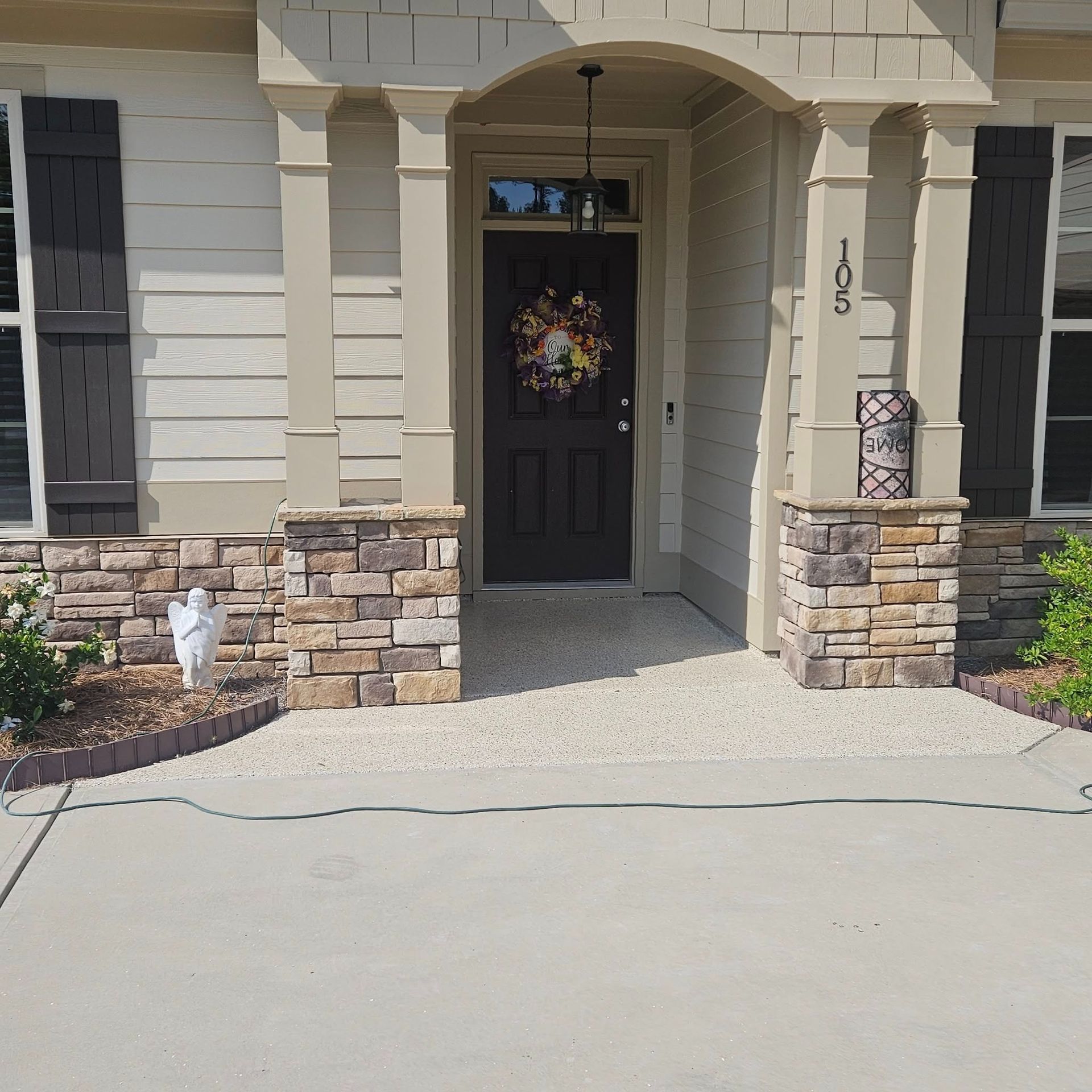 Front entry of a beige house with a black door, stone accents, and a light-colored driveway.
