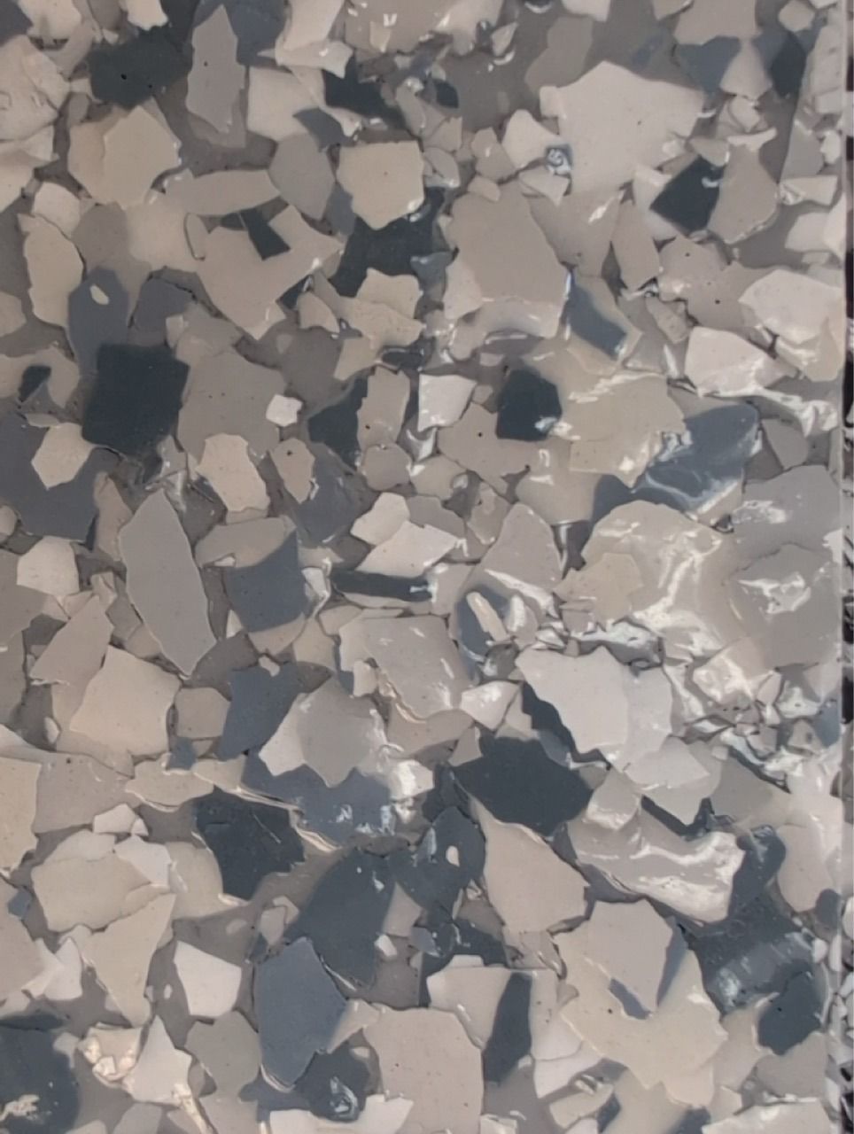 Close-up of gray, beige, and dark blue speckled flooring or chipped paint texture