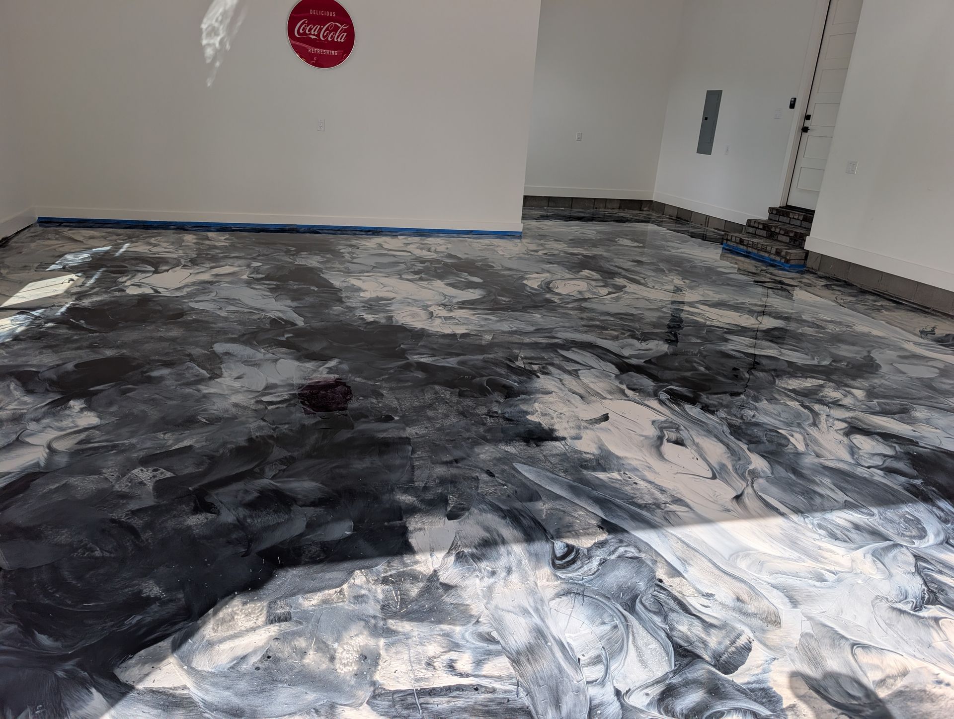 Gray and black stained floor in an unfinished room with white walls and exposed wiring.