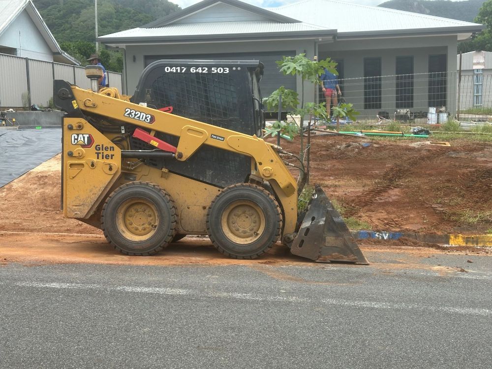 A Yellow Bulldozer Is Driving Through A Dirt Field — Glen Tier Bobcat & Truck Hire In Innisfail, QLD
