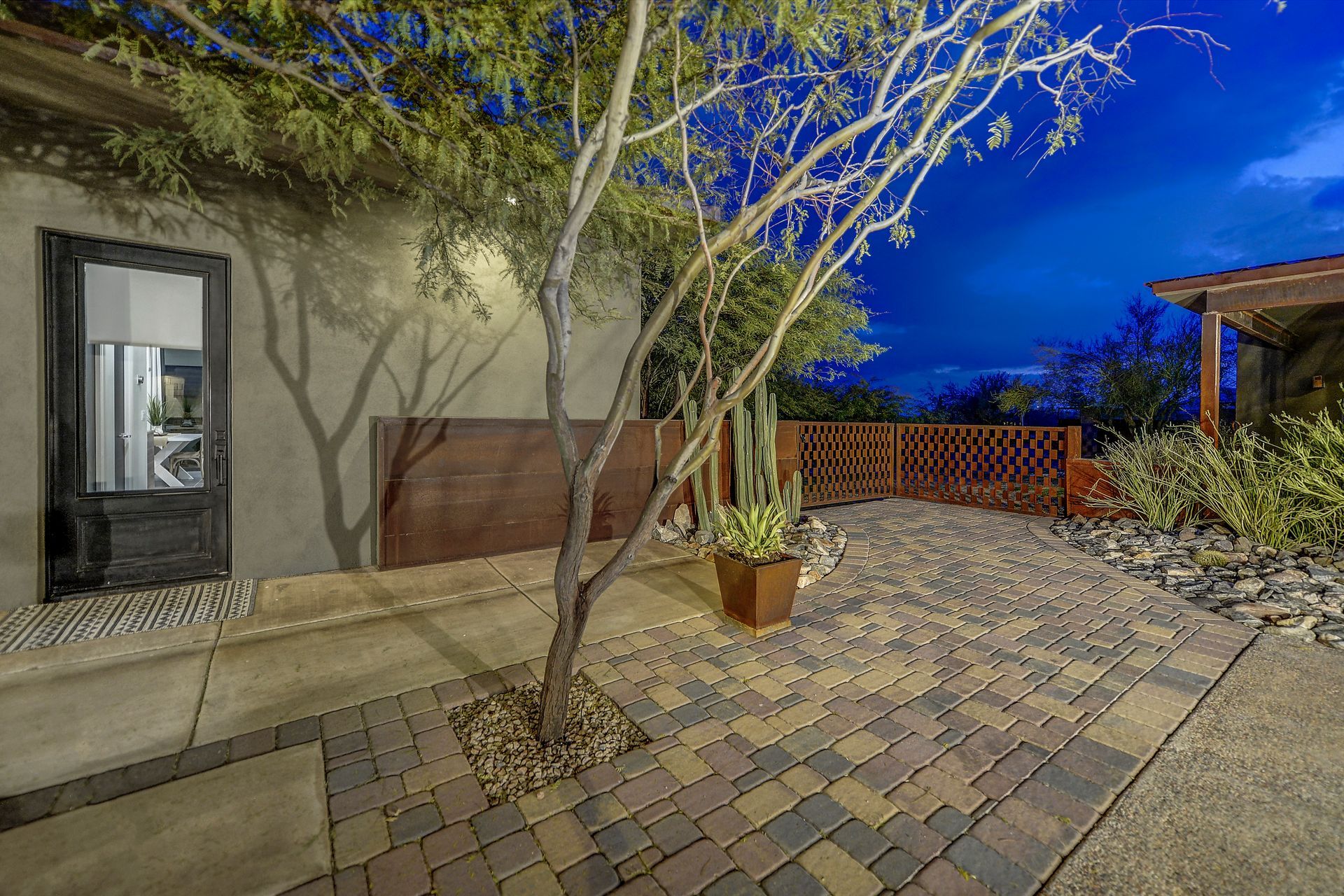 A house with a brick driveway and a tree in front of it at night.