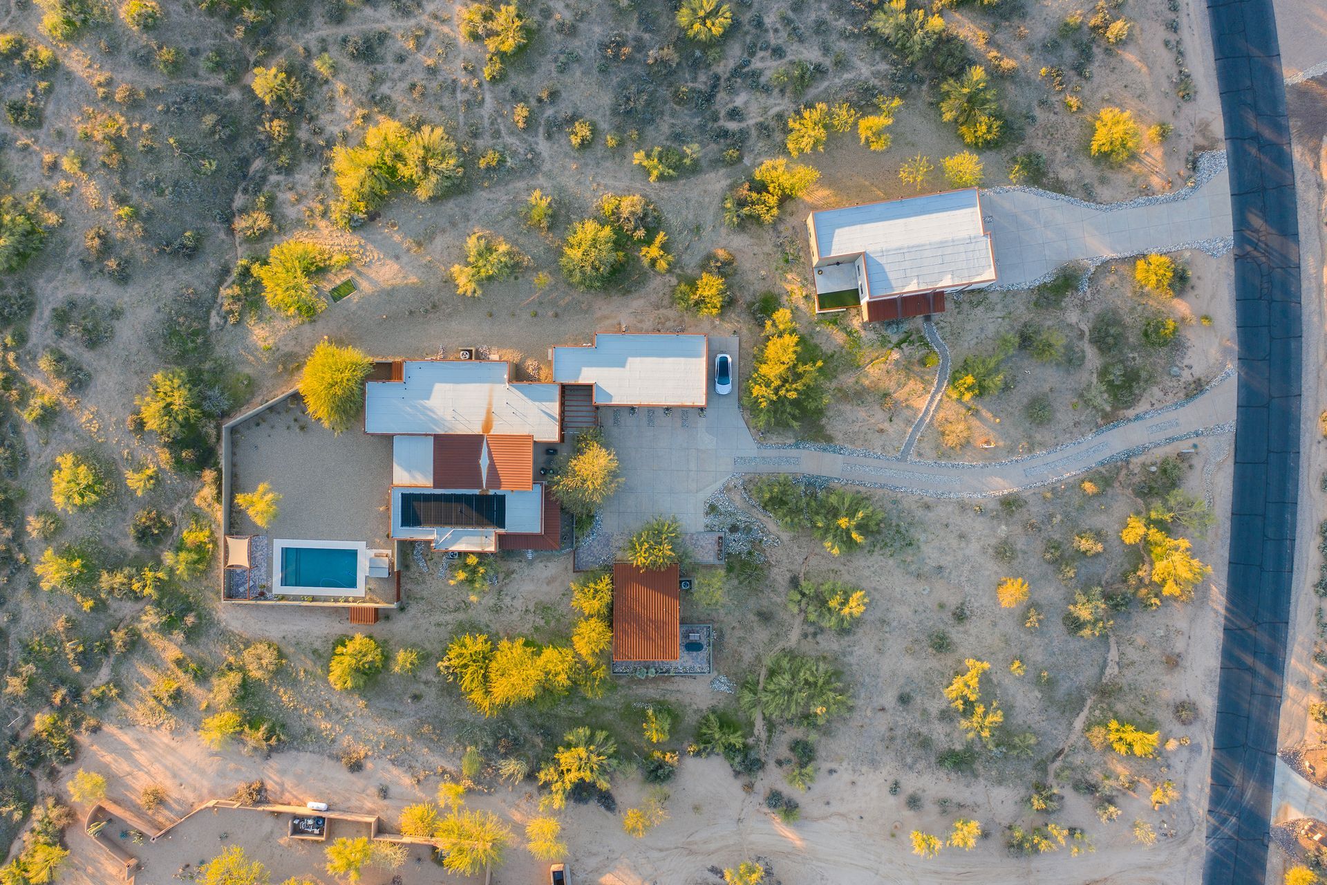 An aerial view of a house in the middle of a desert surrounded by trees.