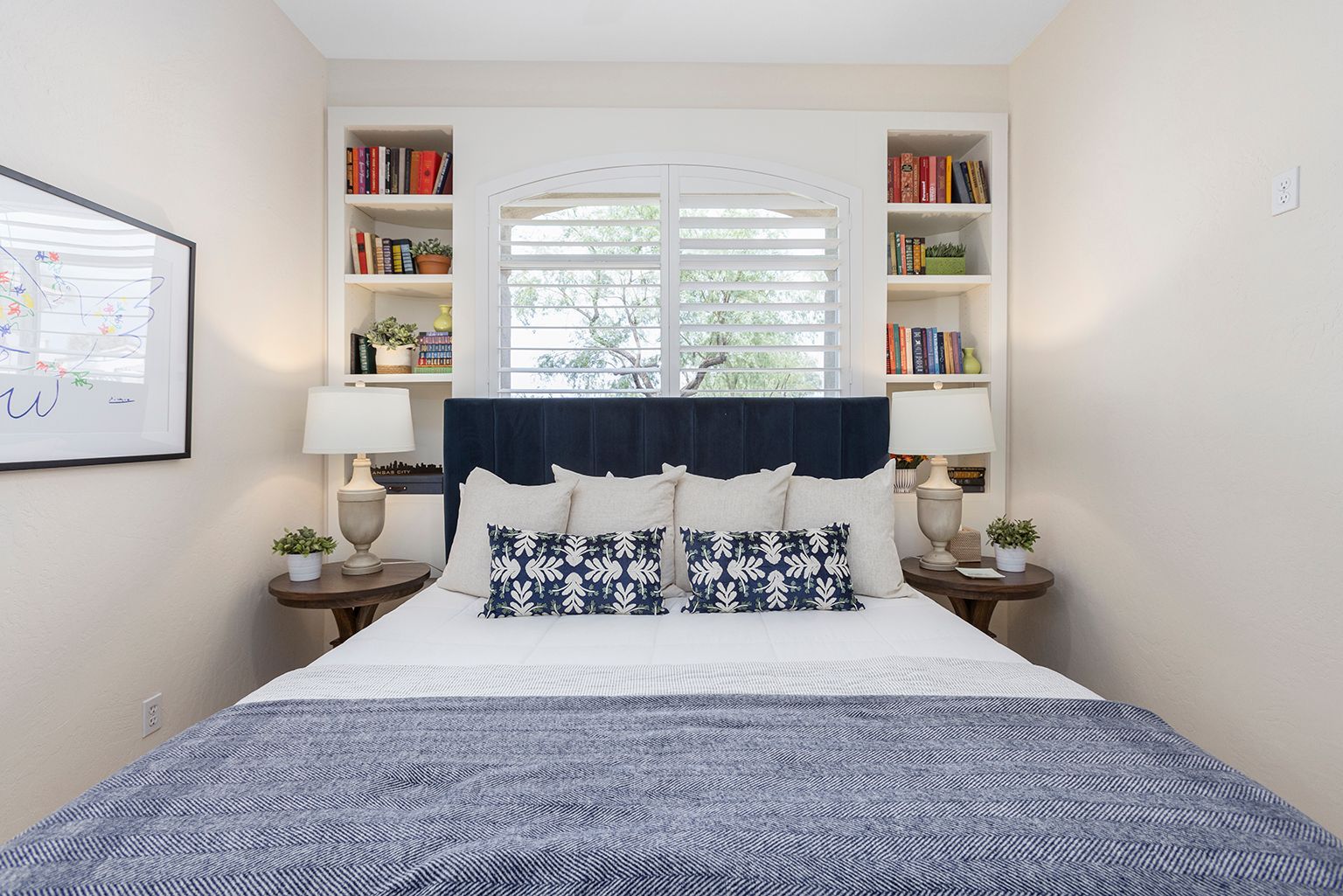 A bedroom with a bed , nightstands , shelves and a window.
