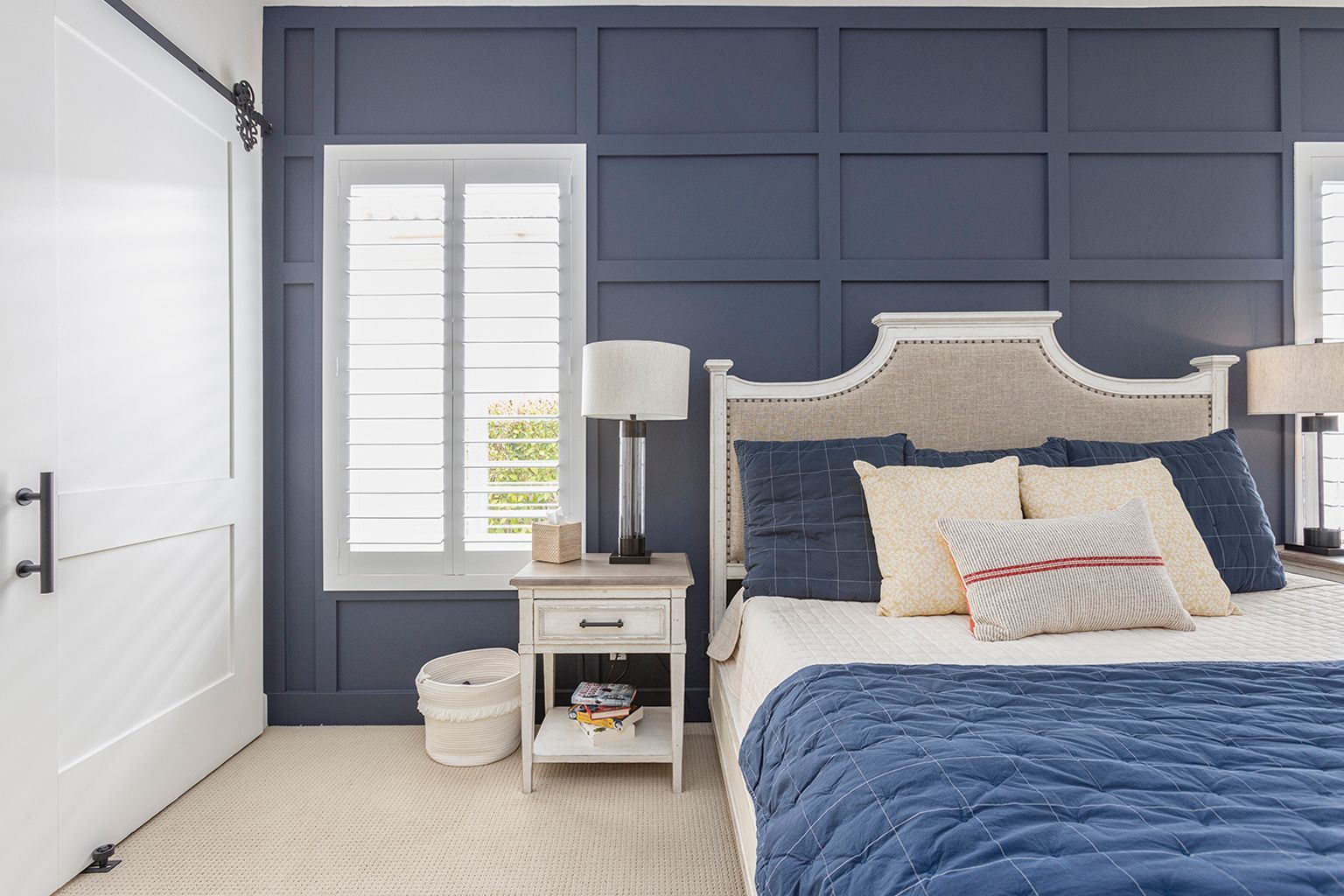 A bedroom with a bed , nightstand , lamps and blue walls.