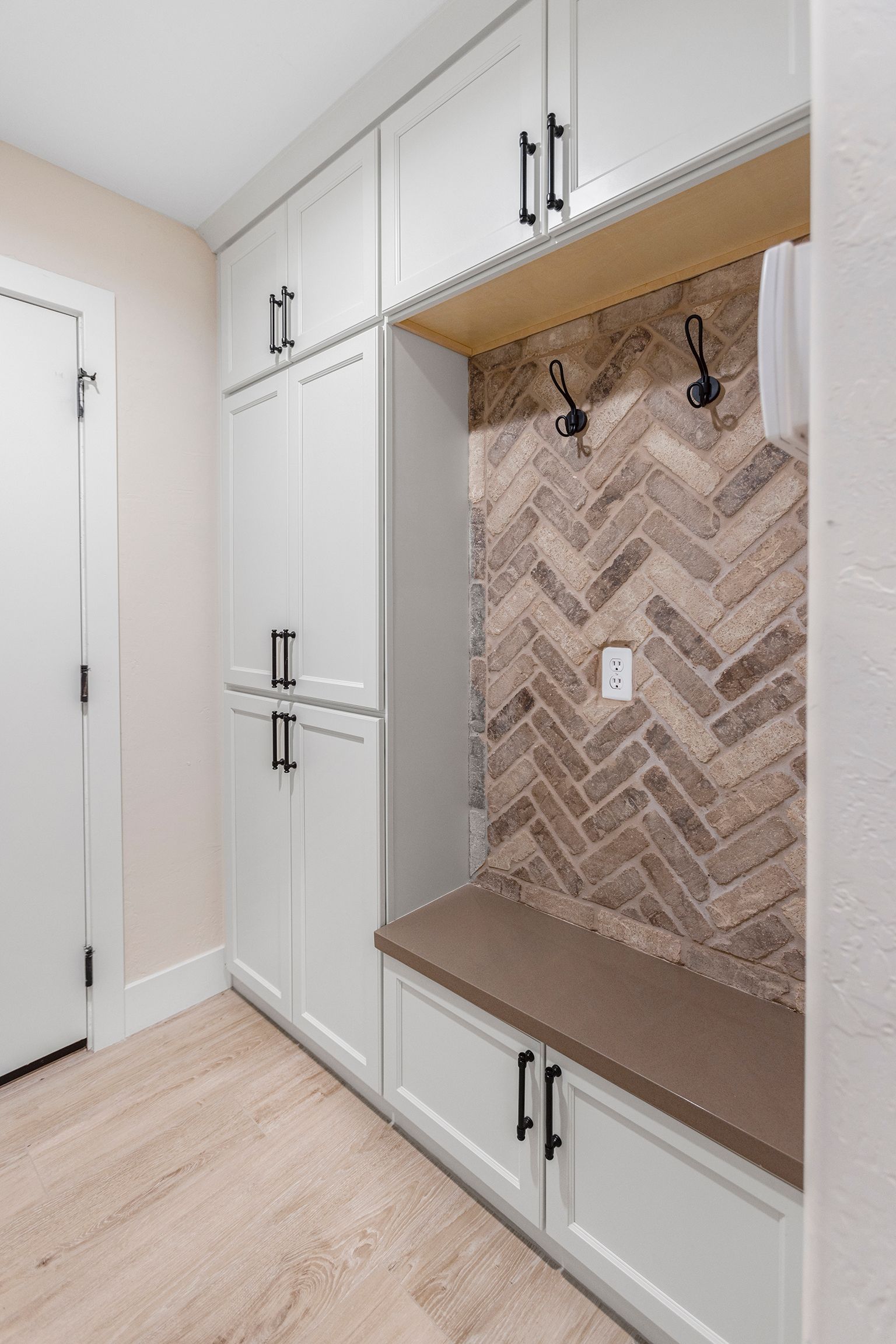 A mud room with white cabinets , a bench , and a brick wall.