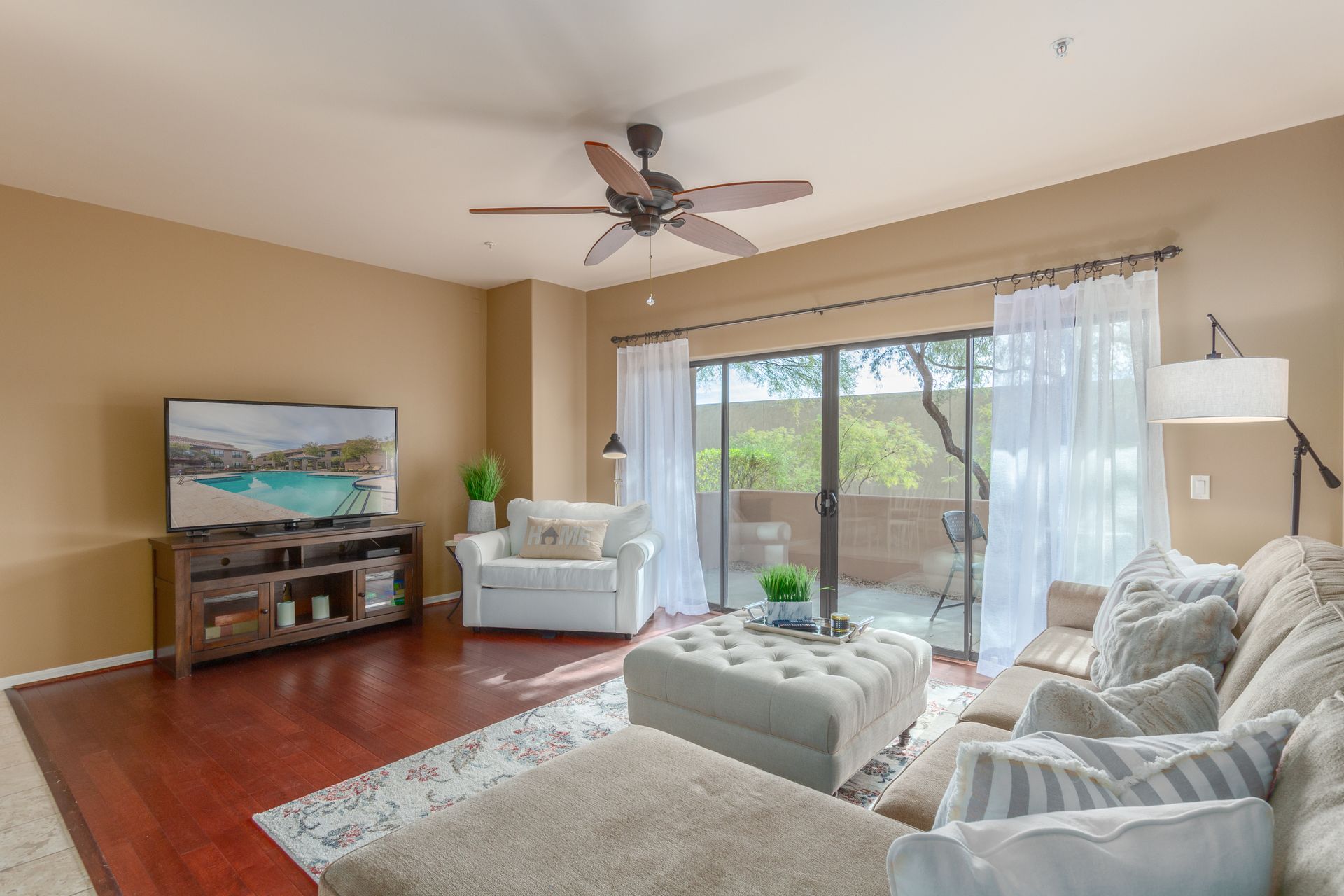A living room with a couch , chair , television and ceiling fan.