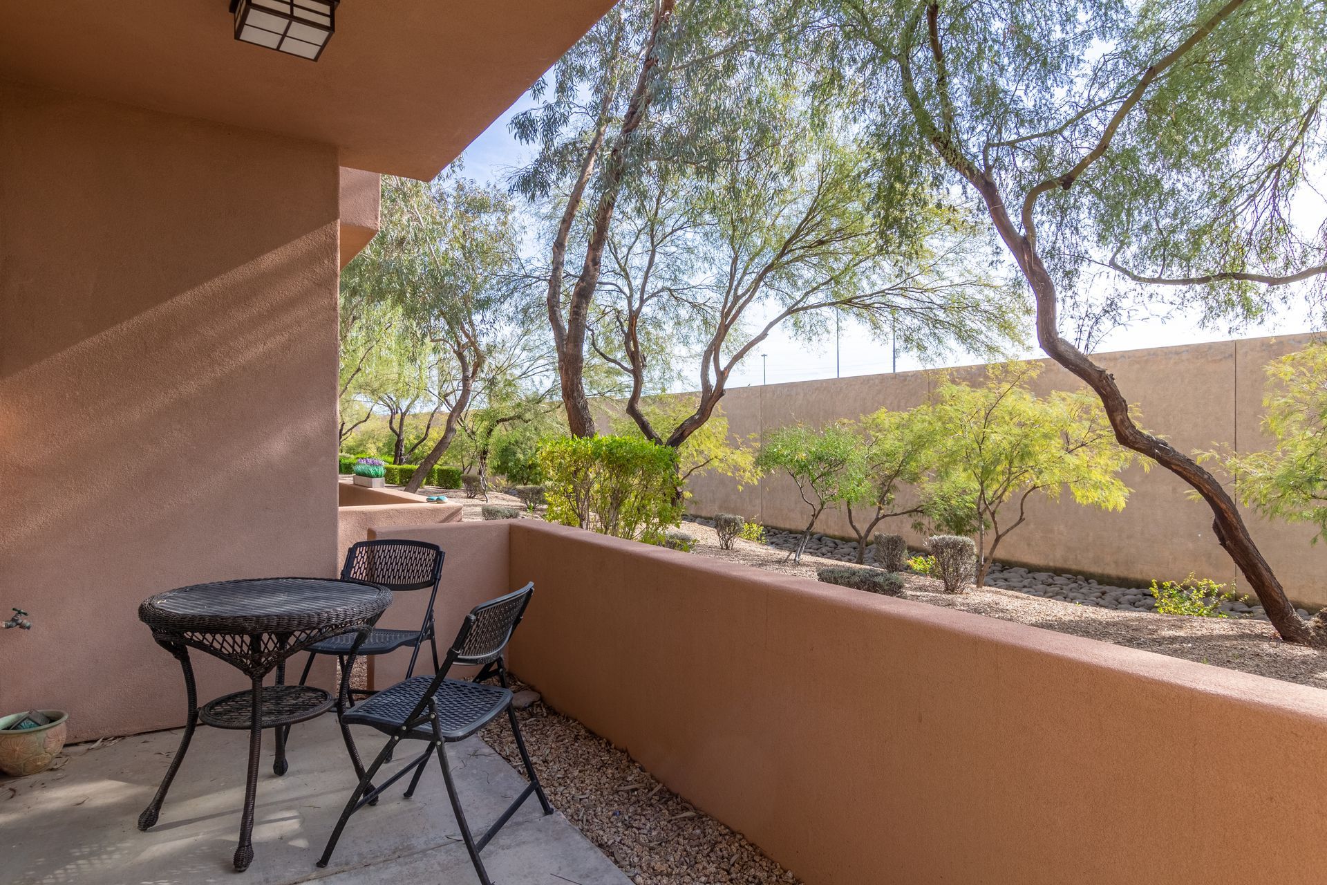 A patio with a table and chairs and trees in the background.