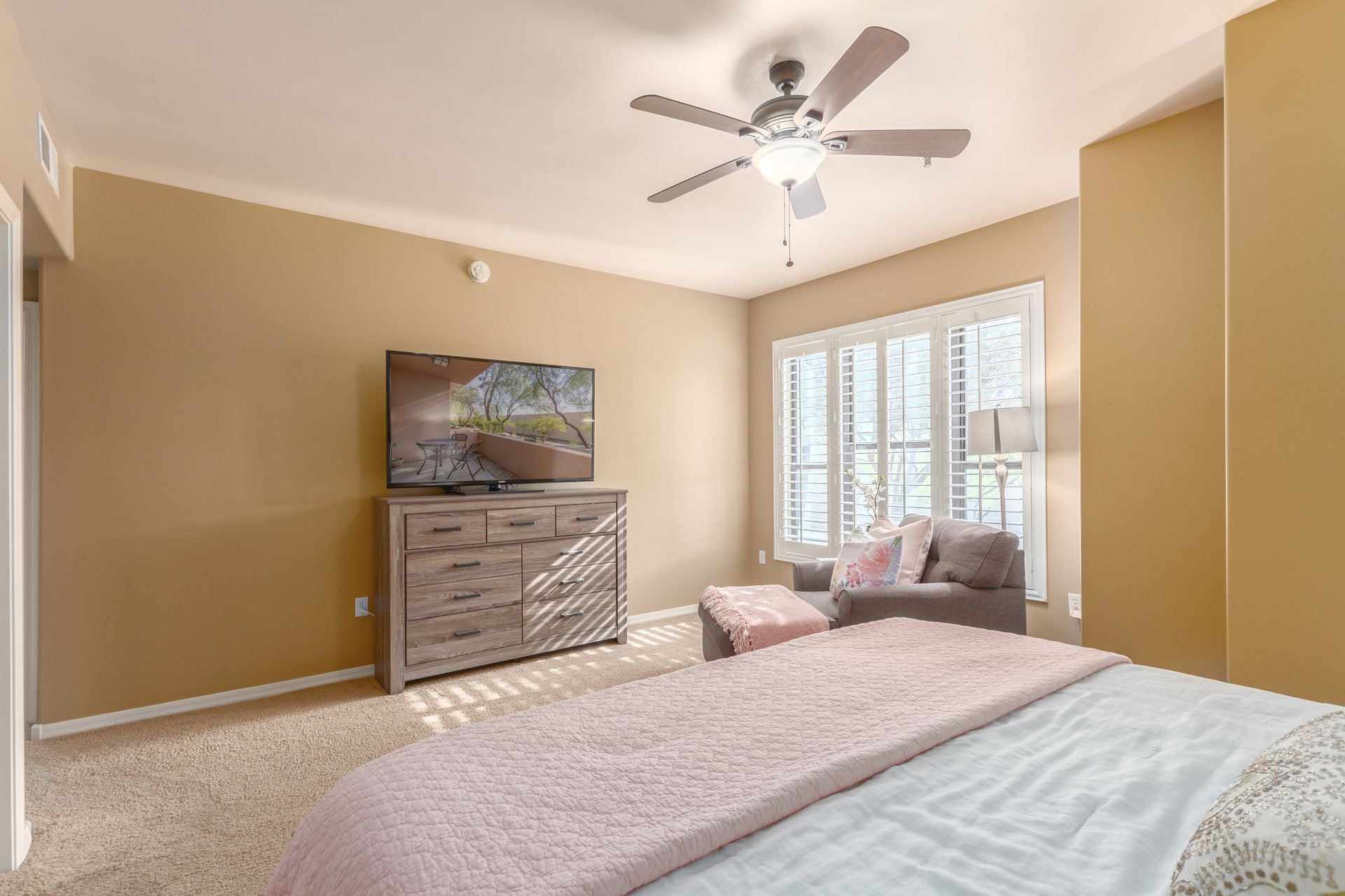 A bedroom with a bed , dresser , television and ceiling fan.