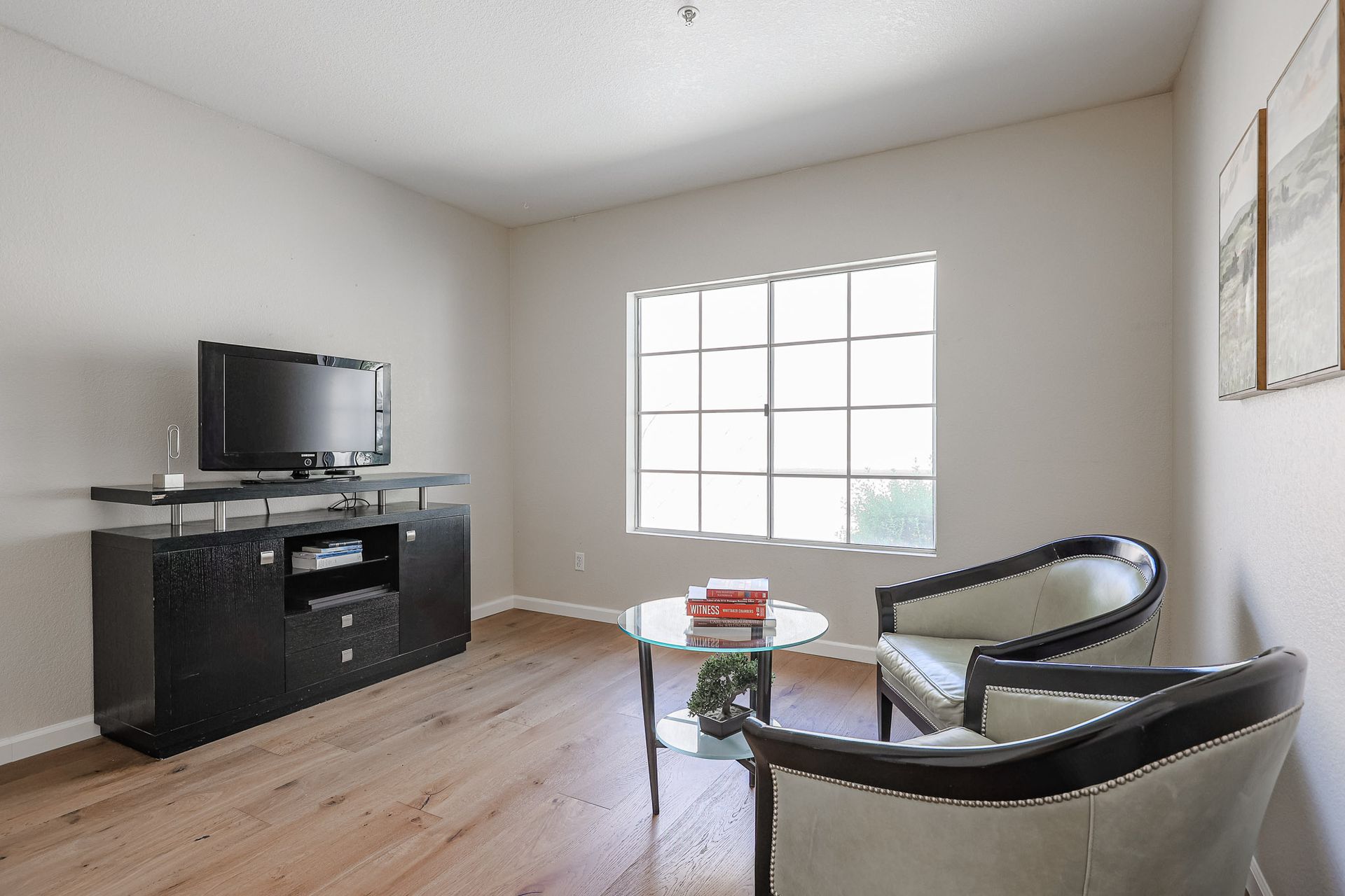 A living room with two chairs , a table , a television and a window.