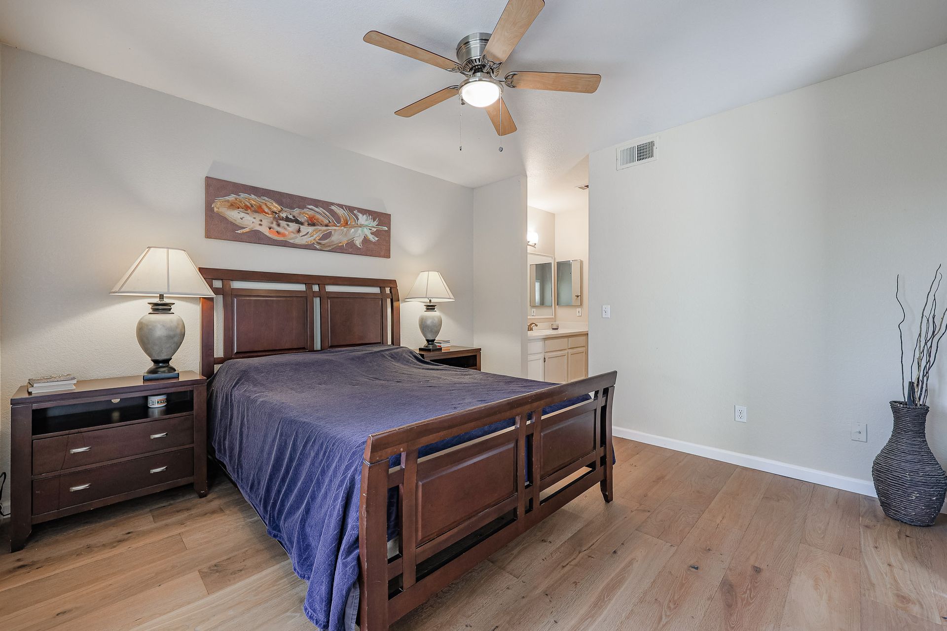 A bedroom with a bed , nightstands , lamps and a ceiling fan.