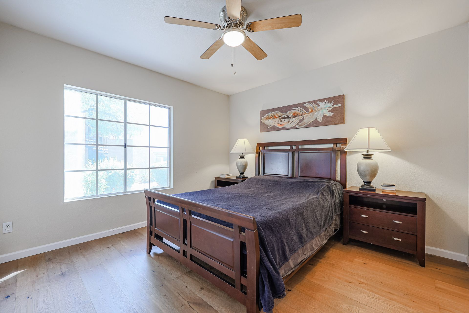 A bedroom with a bed , nightstands , lamps and a ceiling fan.