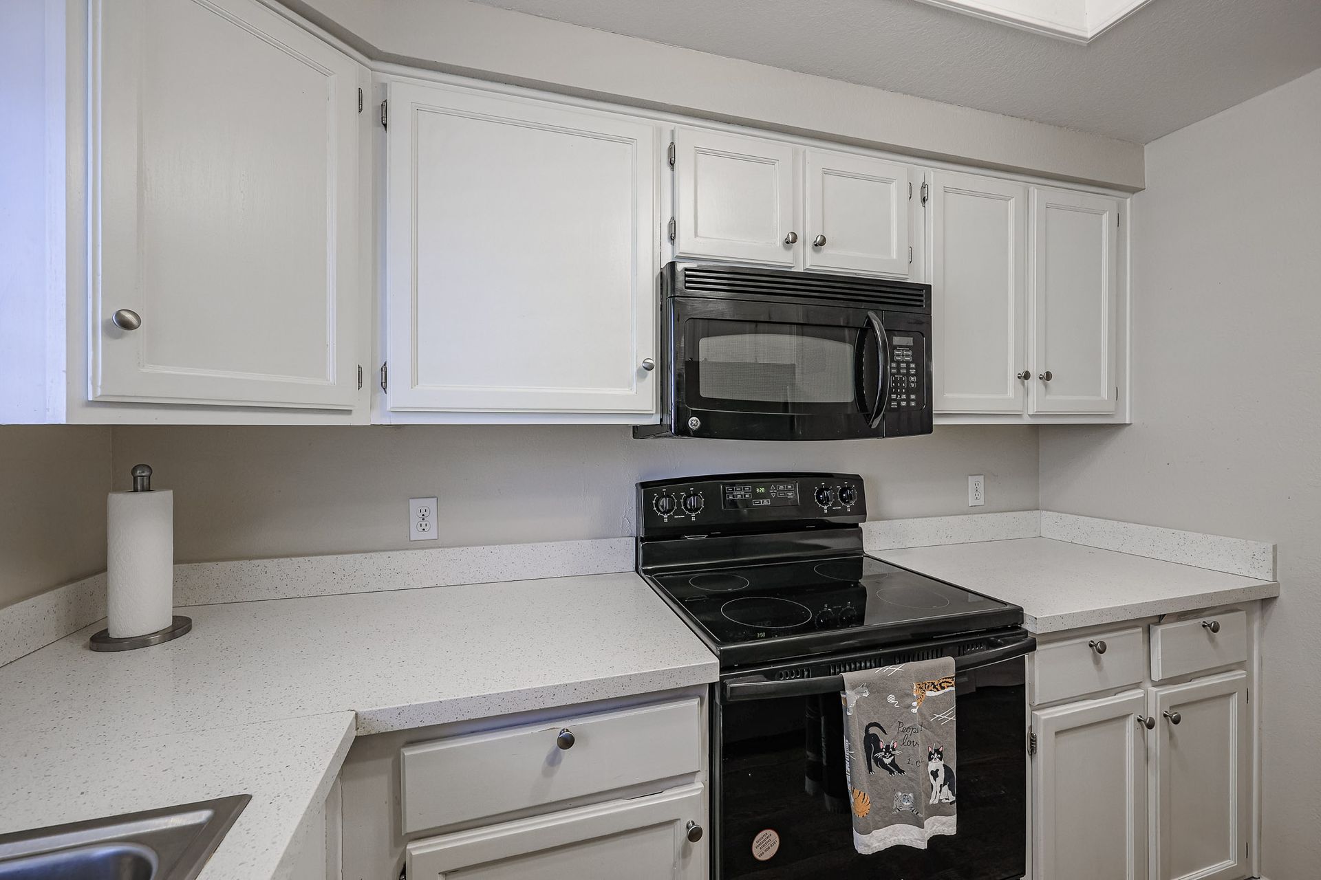 A kitchen with white cabinets , a black stove , a microwave , and a sink.
